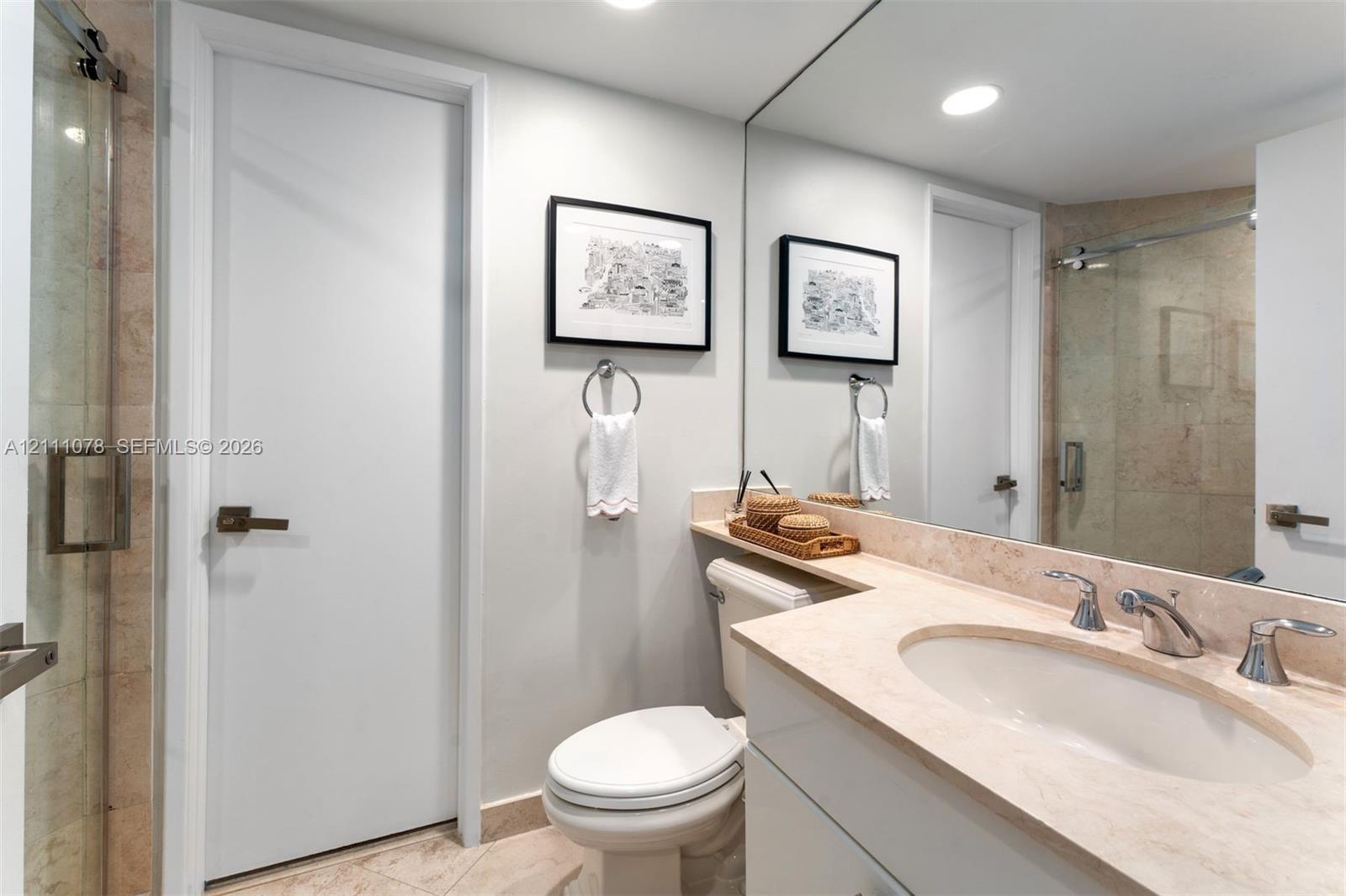 Bathroom featuring a stone-surface vanity with an integrated basin, wall-to-wall mirror, glass-enclosed shower, and light-toned floor tiling