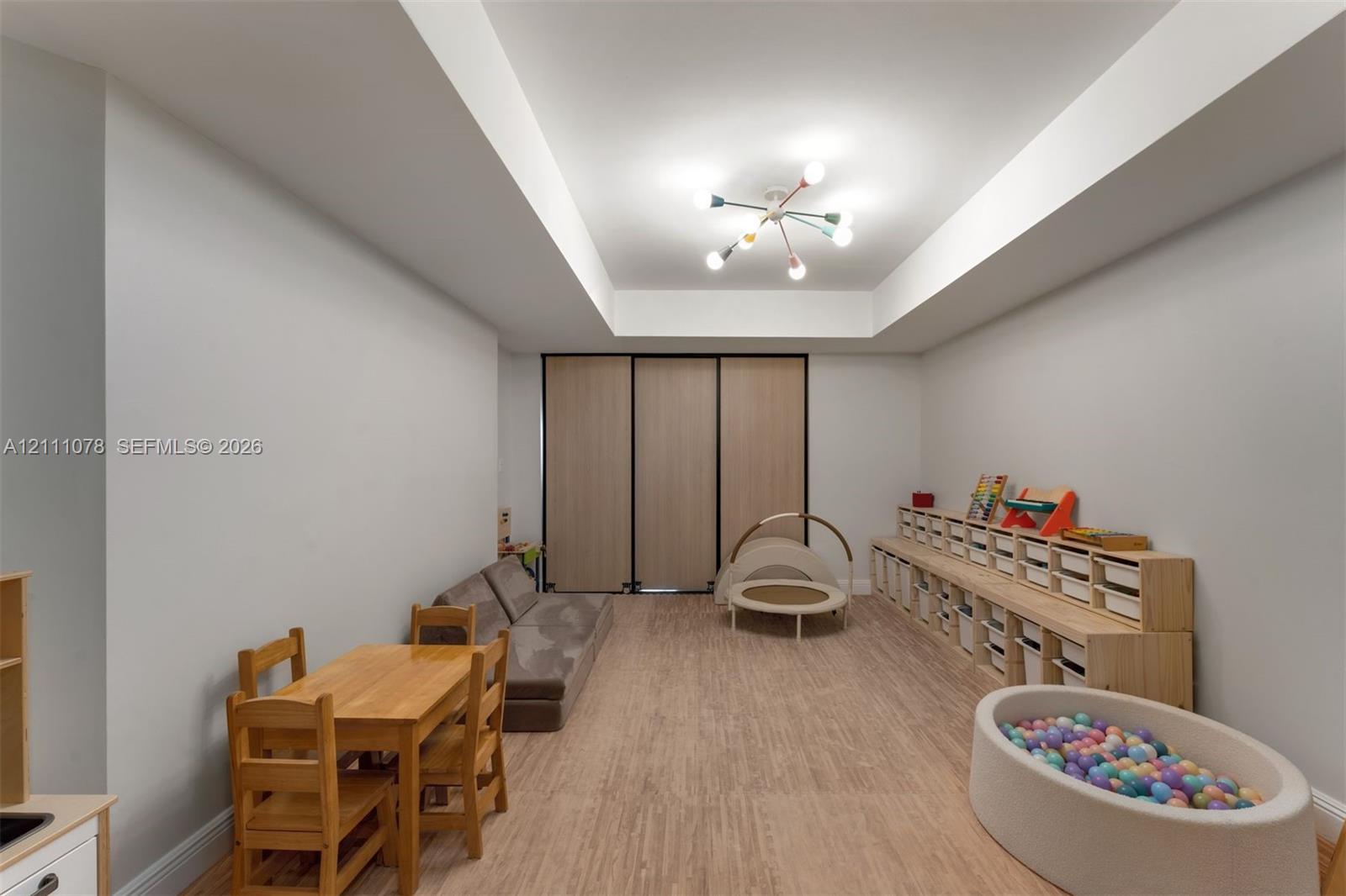 Interior space featuring a recessed tray ceiling, multi-arm light fixture, and wood-finish flooring, accented by floor-to-ceiling built-in wooden storage cabinetry and sleek folding partition doors