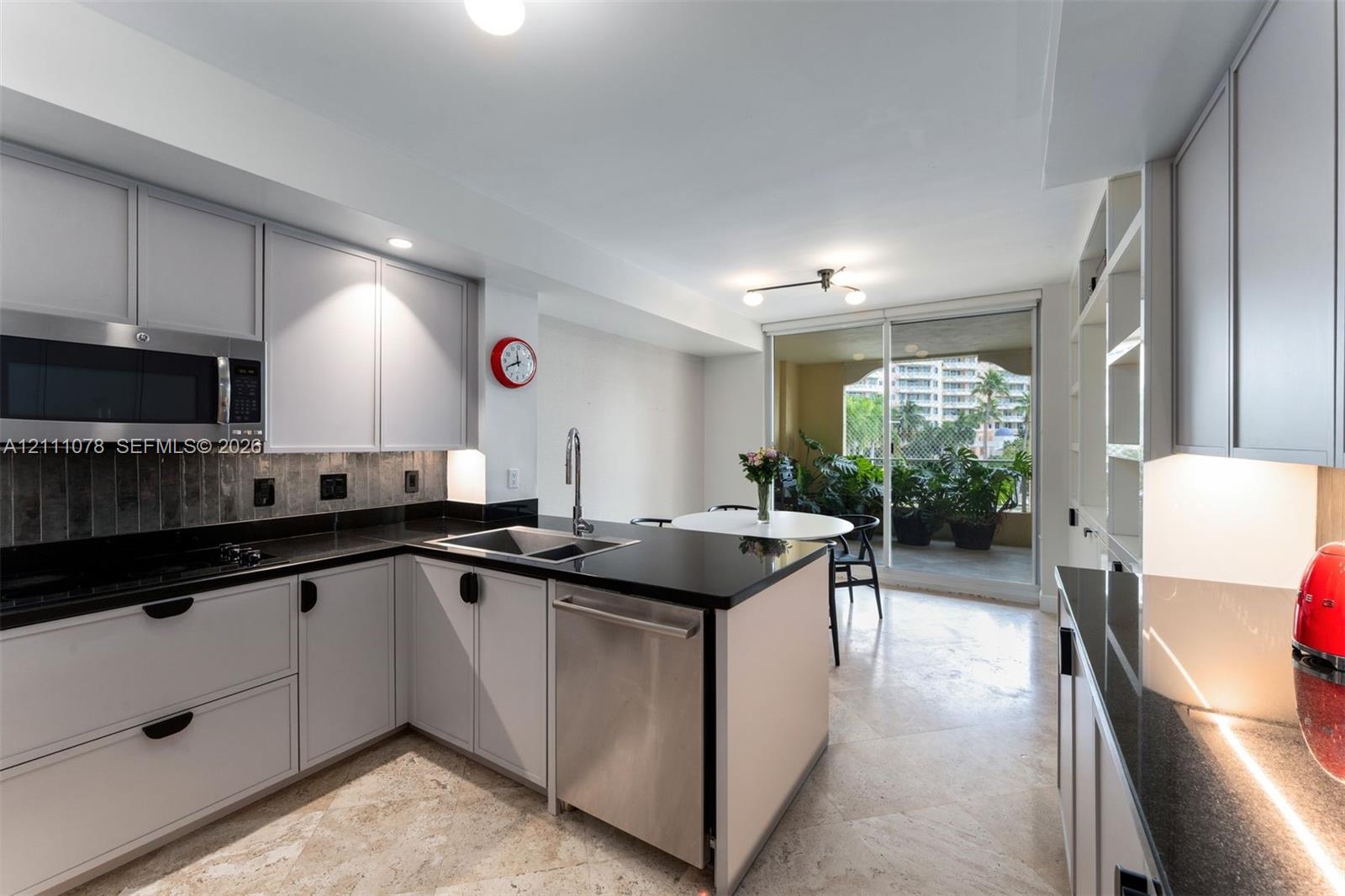 Kitchen featuring light-toned cabinetry, dark stone countertops, stainless steel appliances, built-in shelving, and stone tile flooring