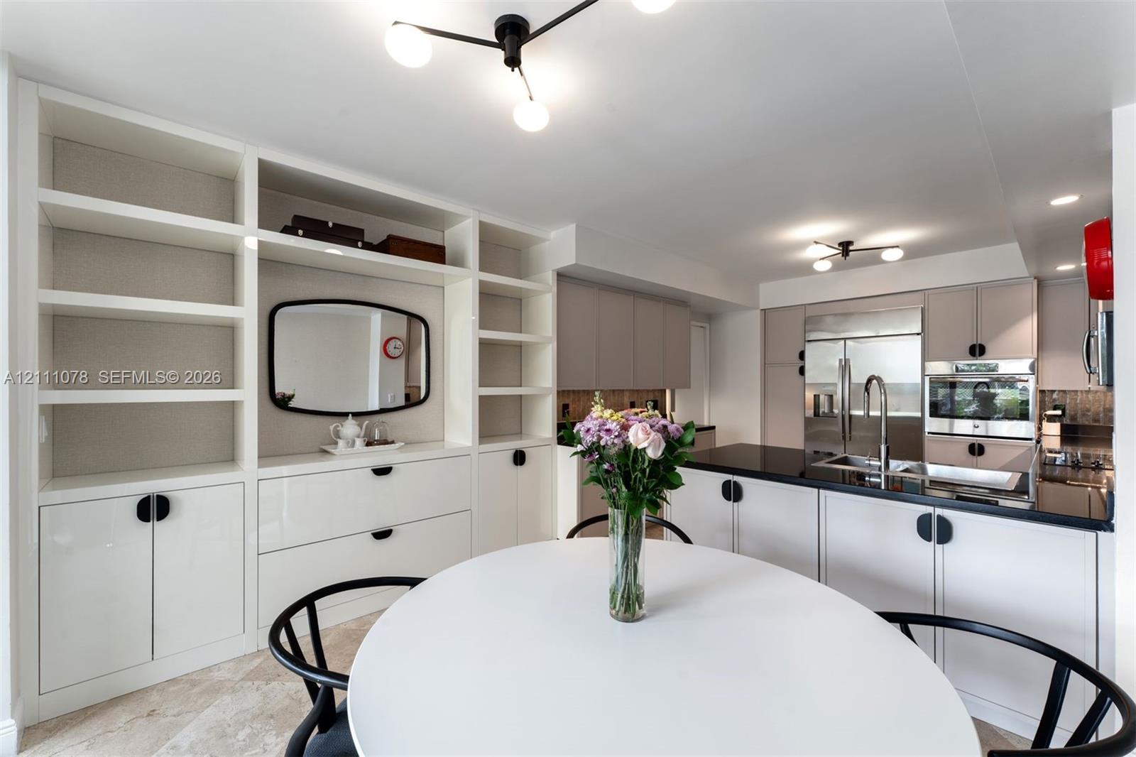 Custom built-in white cabinetry with open shelving, sleek flat-panel kitchen cabinetry, polished dark countertops, stainless steel appliances, and contemporary multi-arm light fixtures