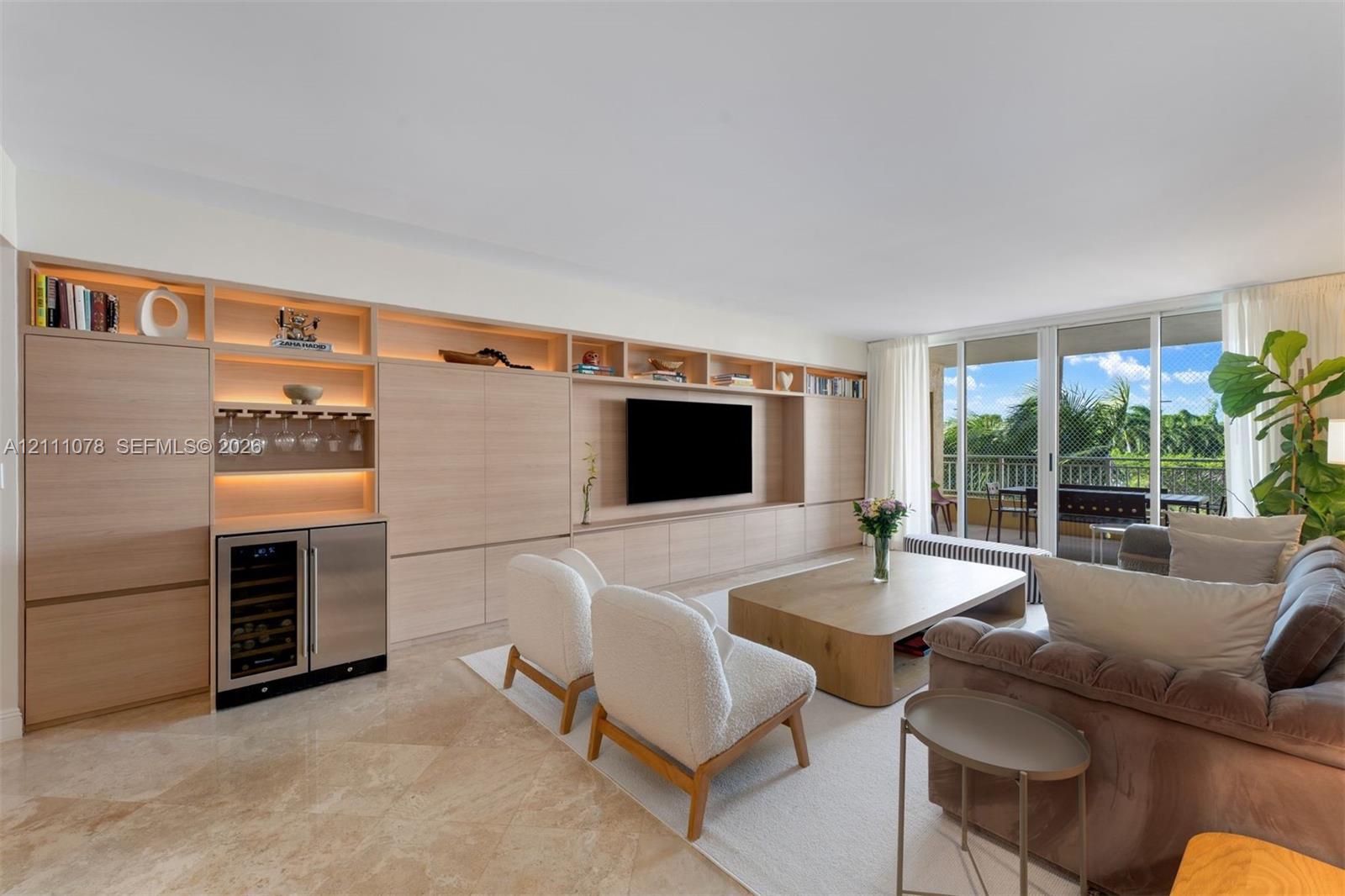 Custom wall-to-wall wood cabinetry with integrated shelving, built-in beverage refrigerator, polished stone flooring, and sliding glass doors opening to a covered balcony