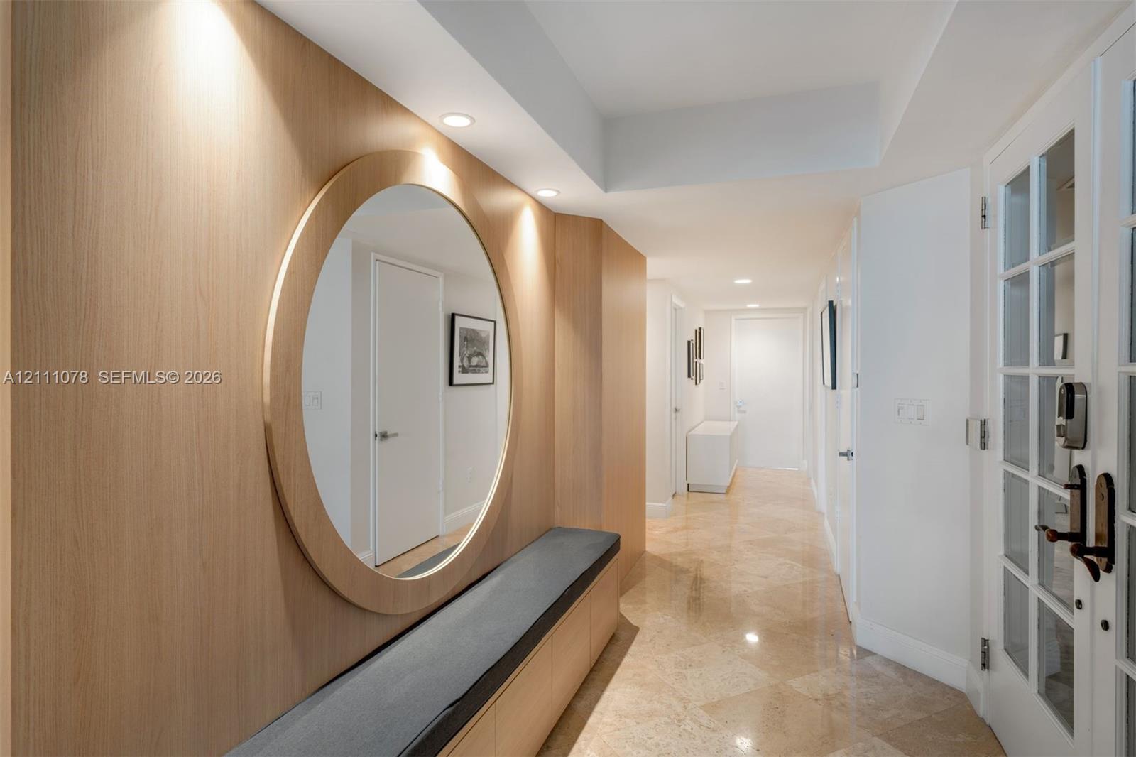 Entryway featuring light-toned wood wall paneling, a large circular mirror, integrated bench seating, stone tile flooring, and recessed ceiling lighting