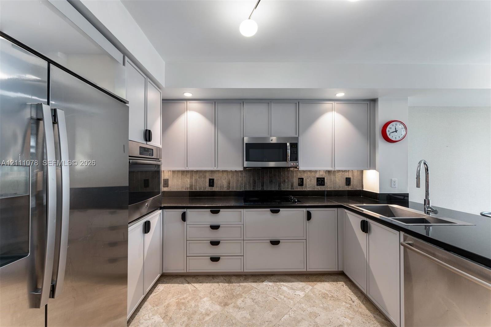 Kitchen featuring stainless steel appliances, neutral cabinetry with dark hardware, stone-finish countertops, tile backsplash, and stone-finish flooring