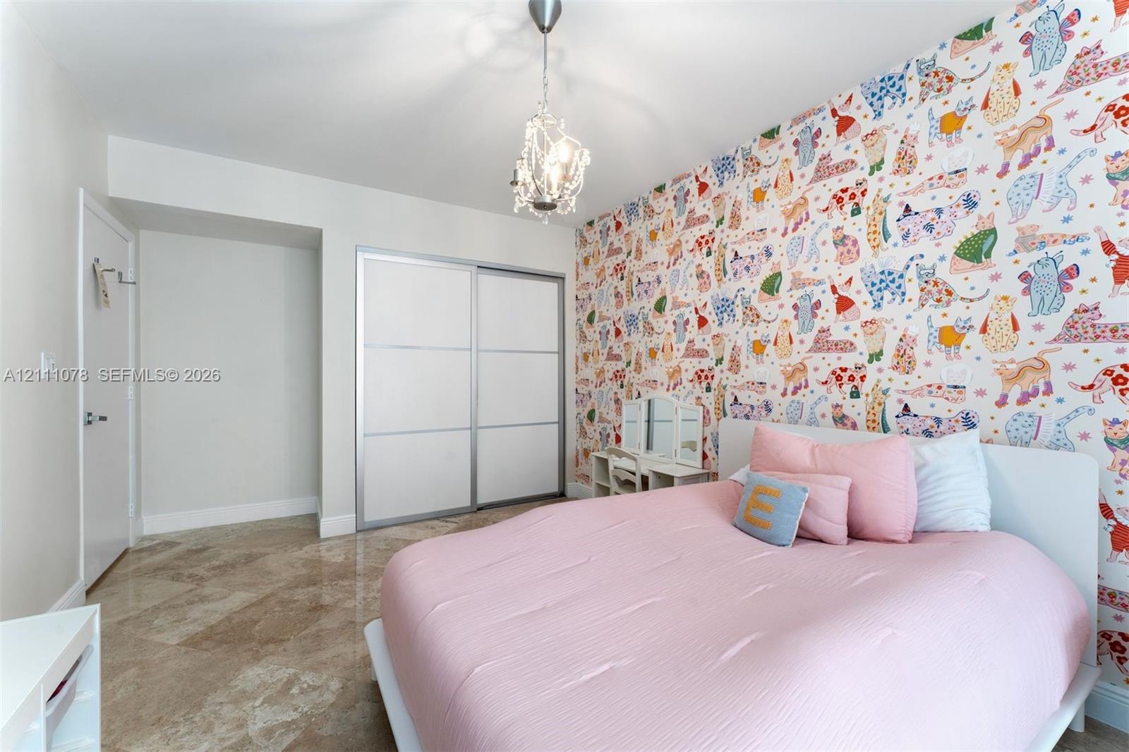Room featuring polished stone flooring, patterned wallpaper accent wall, dual-panel sliding closet doors, and a crystal-style drop pendant light