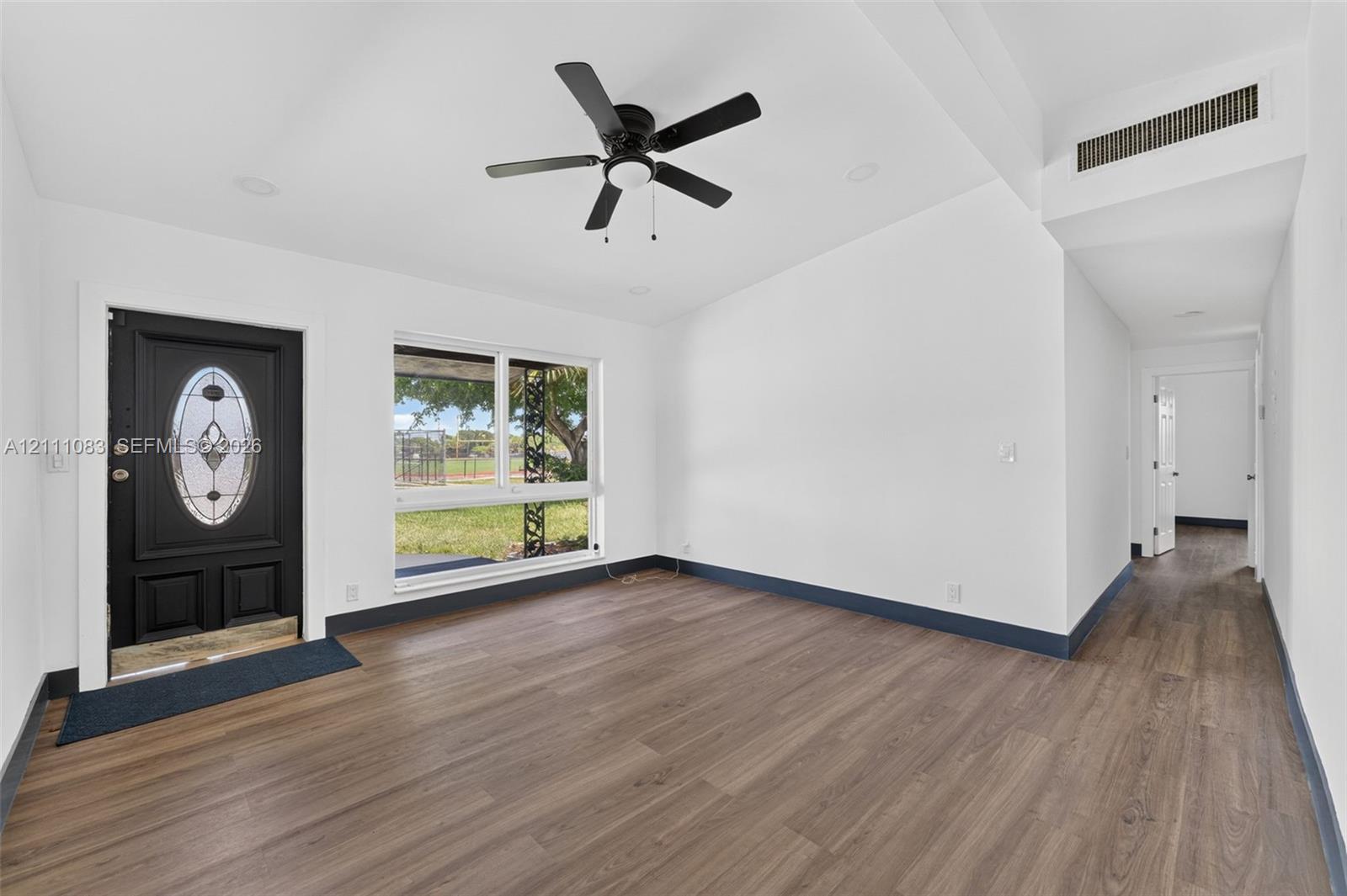 Interior featuring wood-finish flooring, vaulted ceiling, black exterior entry door with glass inlay, large window, and ceiling fan
