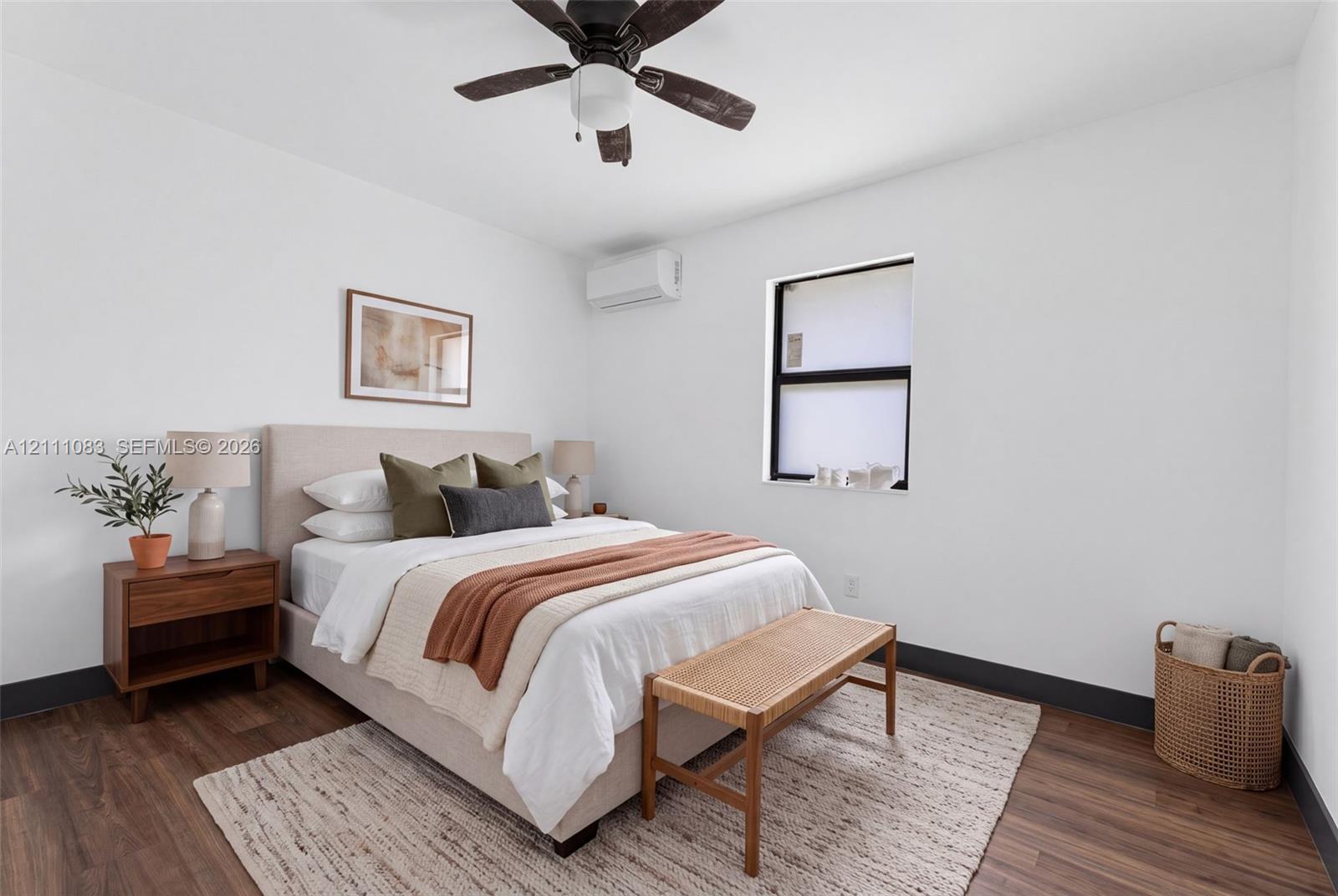 Room featuring wood-finish flooring, a wall-mounted ductless air conditioning unit, a ceiling fan, and a window with a black frame