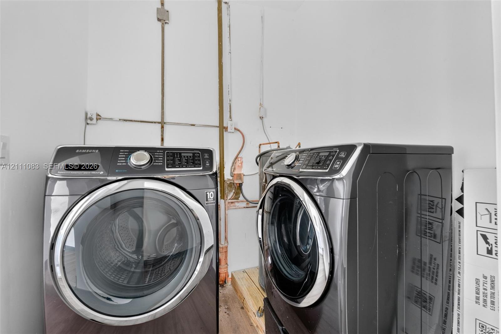 Laundry area featuring front-loading appliances, exposed plumbing, and wood-finish flooring