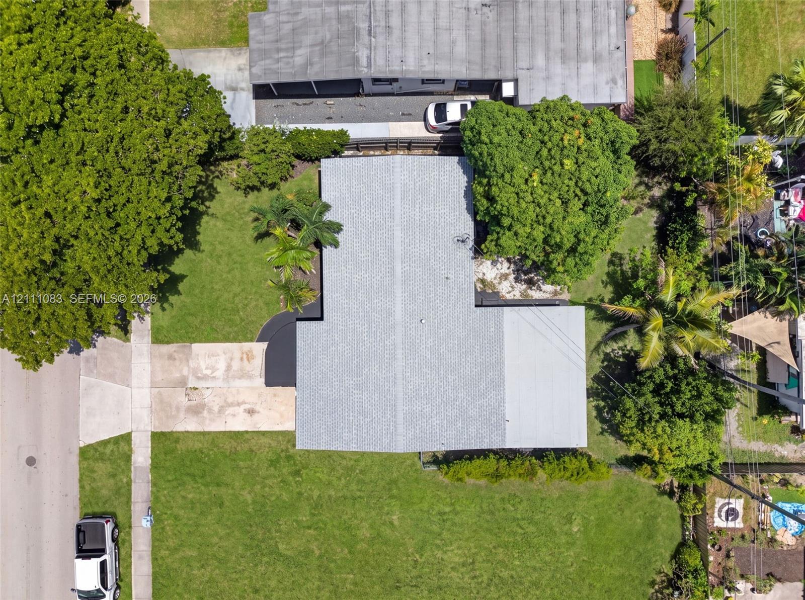 Aerial view featuring a paved driveway, expansive lawn, mature tree canopy, and established landscaping