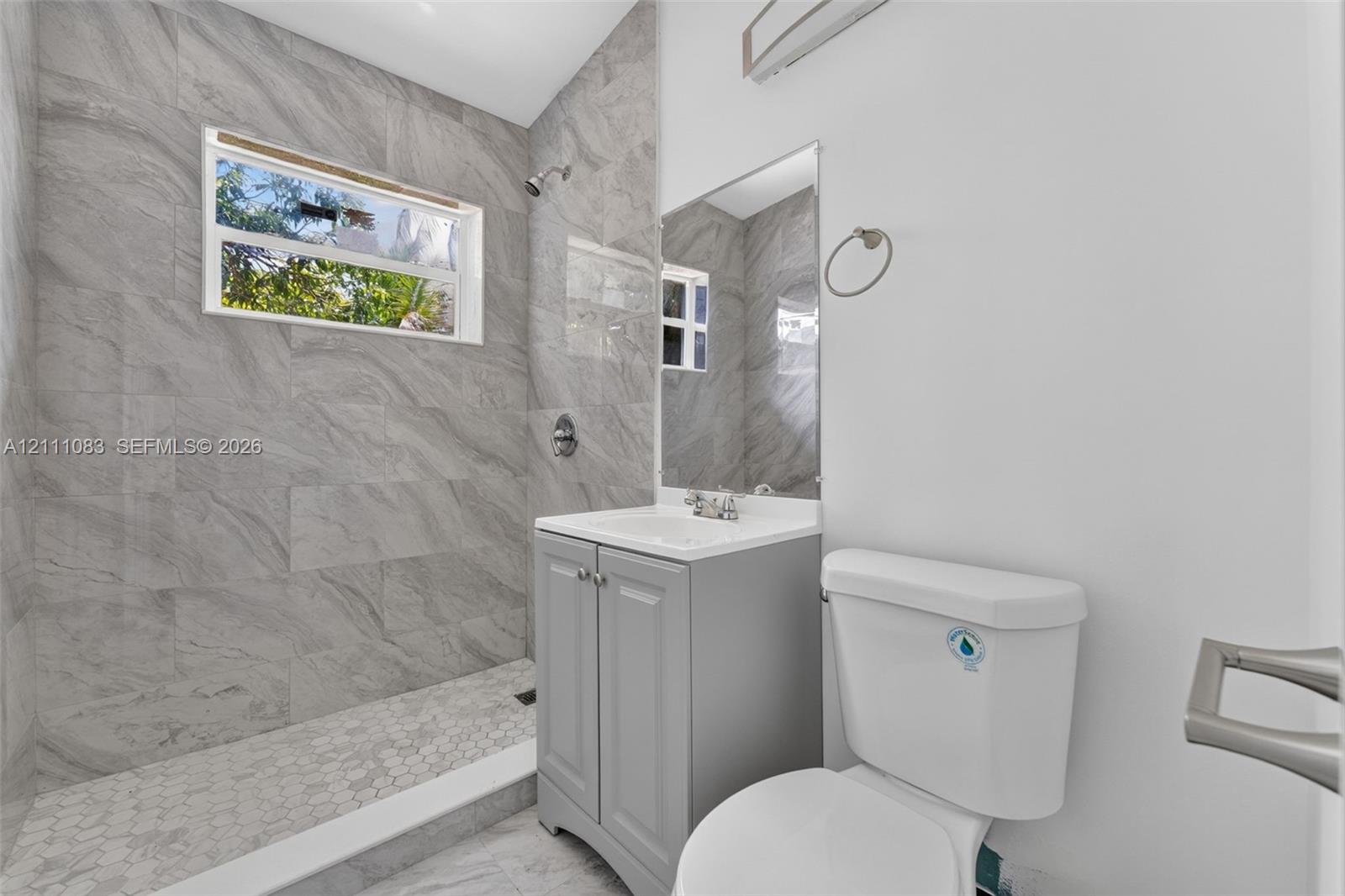 Bathroom featuring floor-to-ceiling gray tile shower walls, hexagonal tile shower flooring, and a grey single-sink vanity