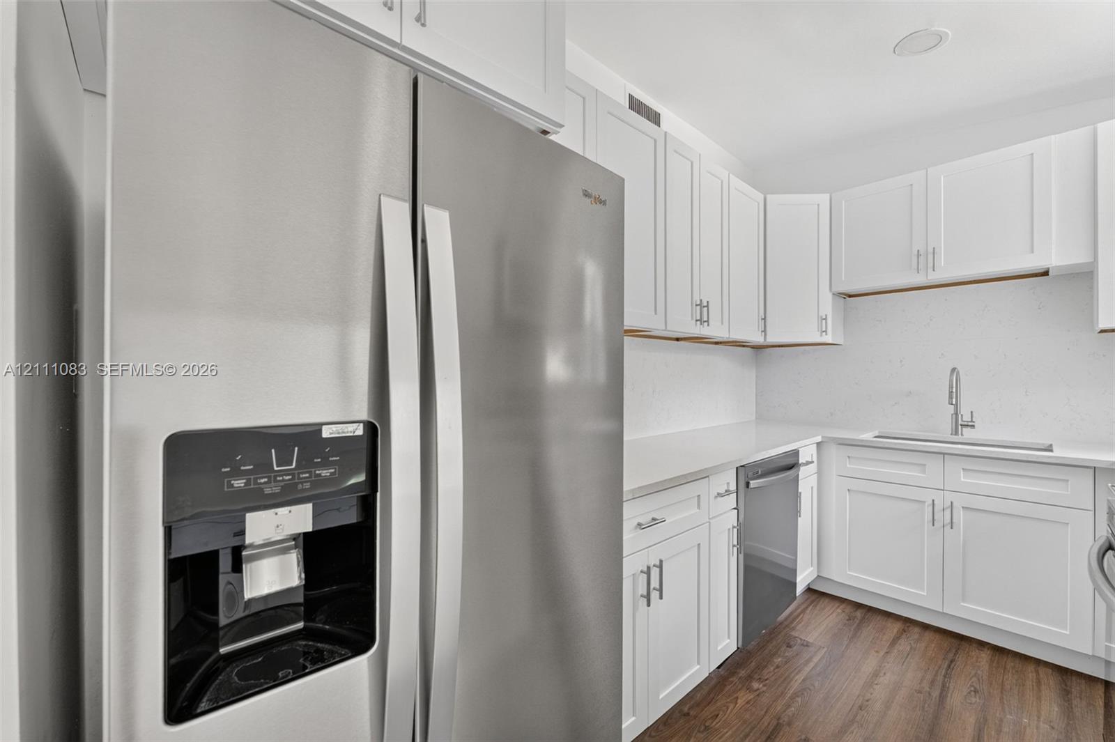 Kitchen featuring stainless steel appliances, shaker-style cabinetry, solid-surface countertops, undermount sink with a gooseneck faucet, and wood-finish flooring