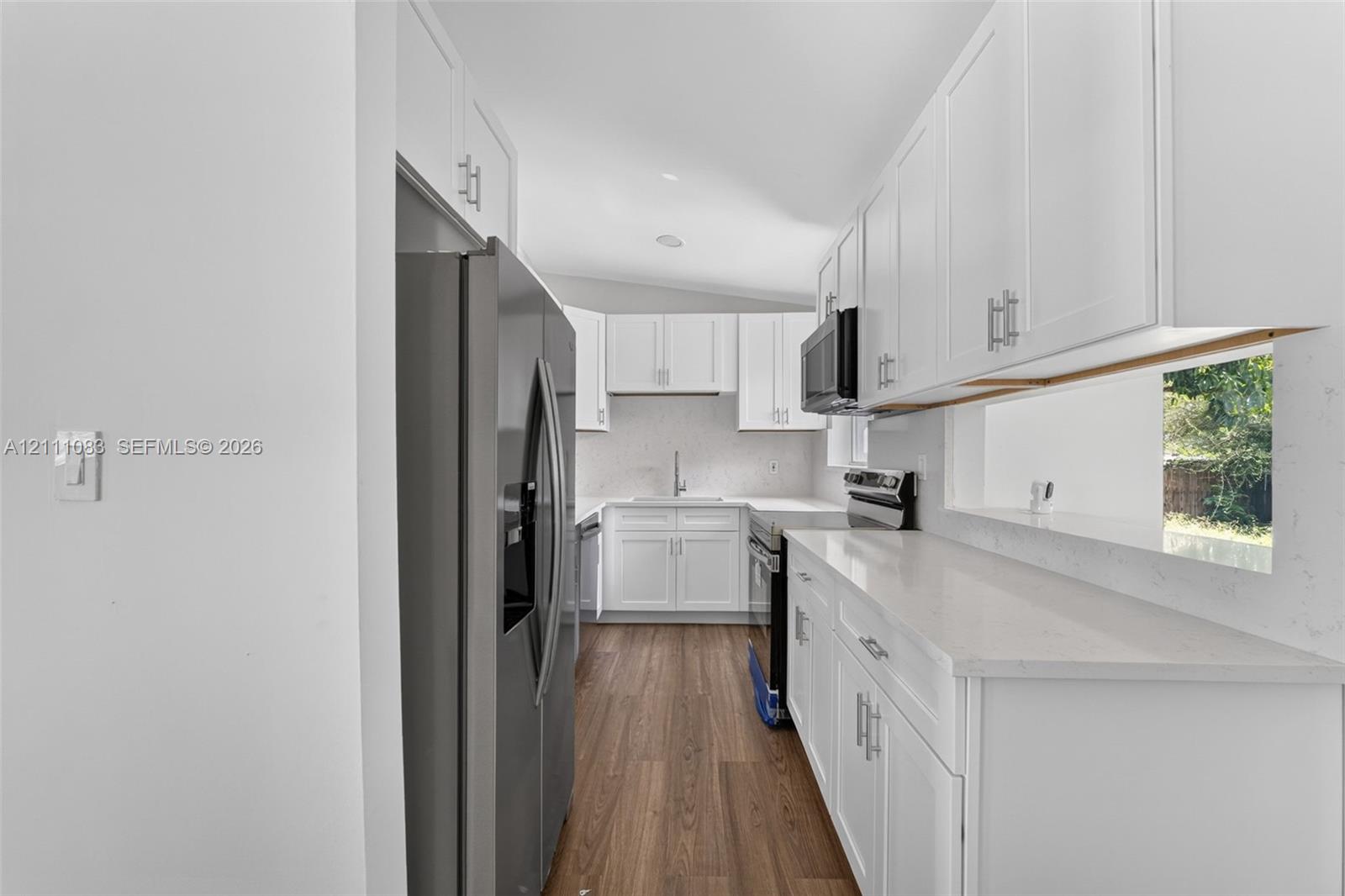 Kitchen featuring white shaker-style cabinetry, solid-surface countertops, wood-finish flooring, and stainless steel appliances