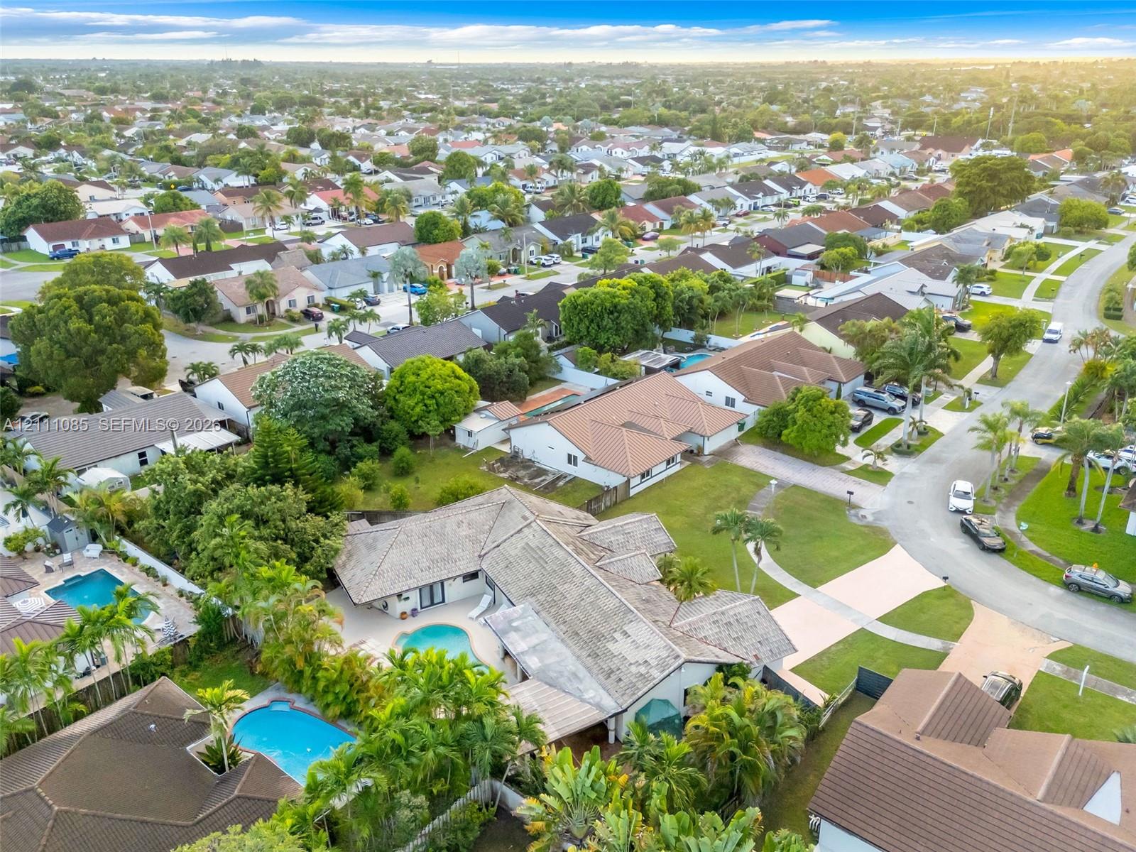 Aerial perspective of a residential property featuring a tiled roof, an in-ground swimming pool, a concrete patio area, and mature landscaping