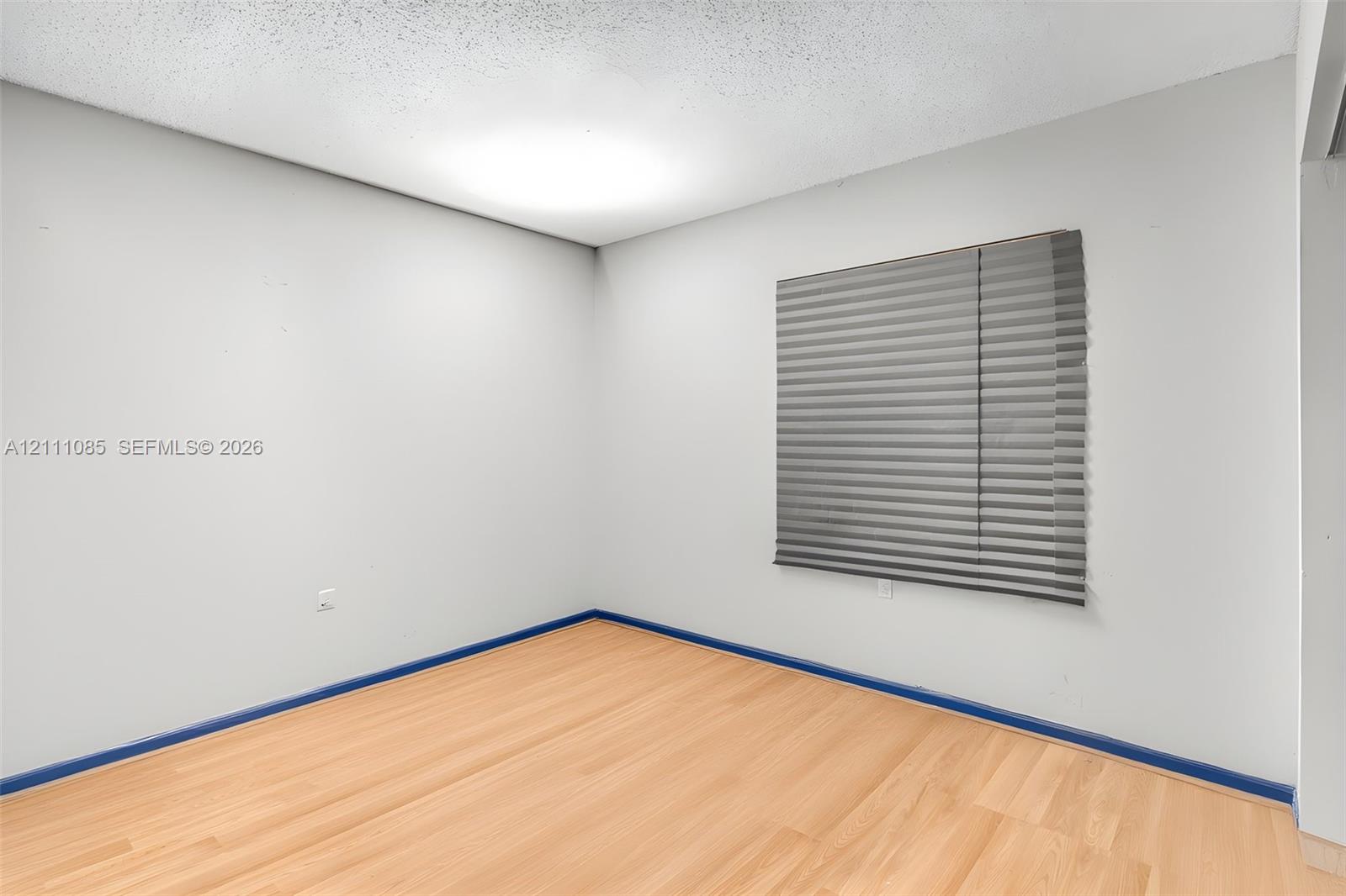 Interior space featuring light-toned wood-finish flooring, neutral wall coloring, and a window with horizontal blinds