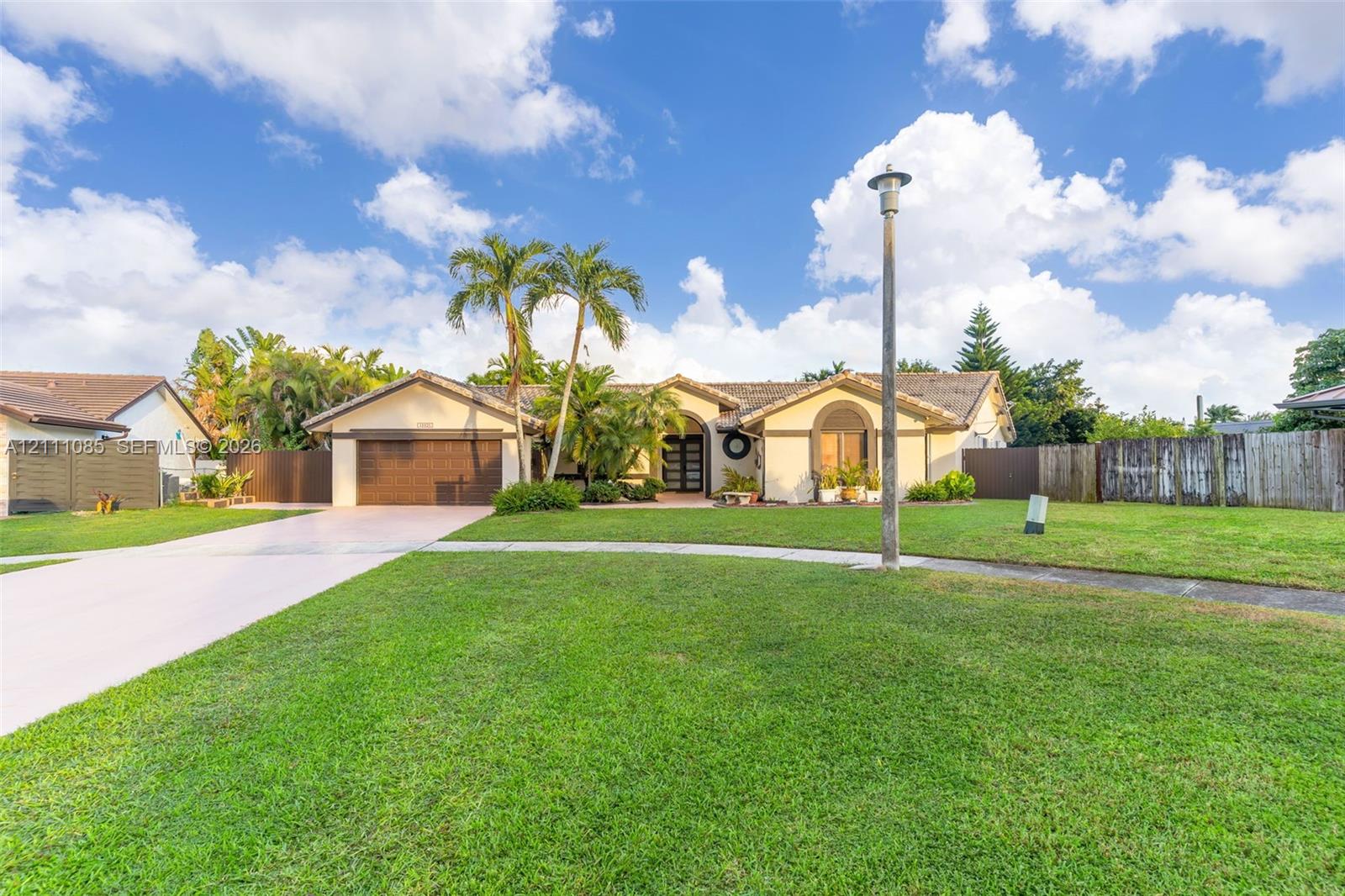 Single-story residence featuring a tile roof, light-colored stucco exterior, arched entryway, wooden garage door, and a spacious front lawn Single-story residence featuring a tile roof, light-colored stucco exterior, arched entryway, wooden garage door, and a spacious front lawn