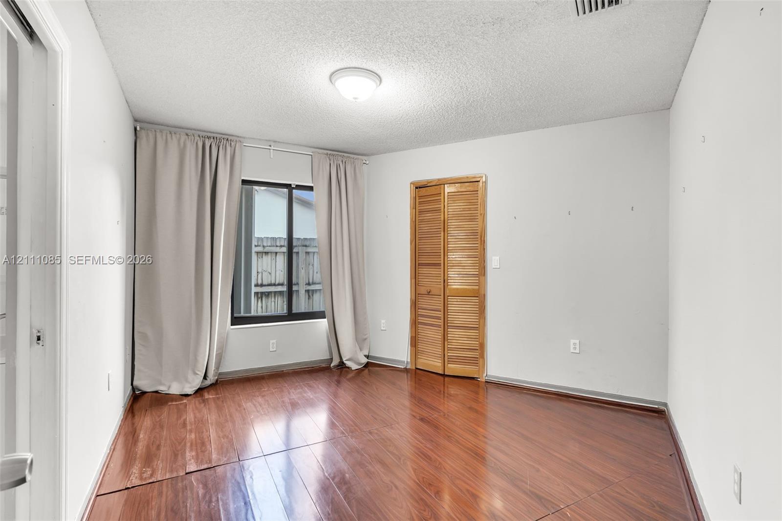 Room featuring wood-finish flooring, a window with a black frame, and a bi-fold wooden closet door