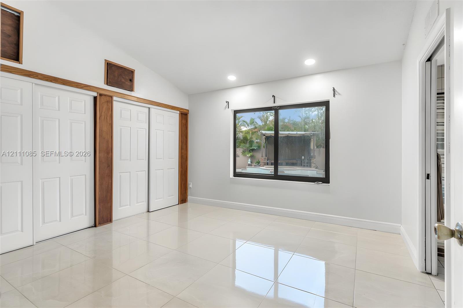 Room featuring large-format tile flooring, vaulted ceiling, dual sliding-door closets with natural wood-tone trim, and recessed lighting