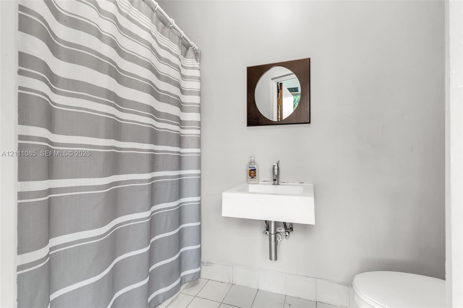 Wall-mounted rectangular basin with a single-handle chrome faucet, square wood-framed mirror, and tiled flooring