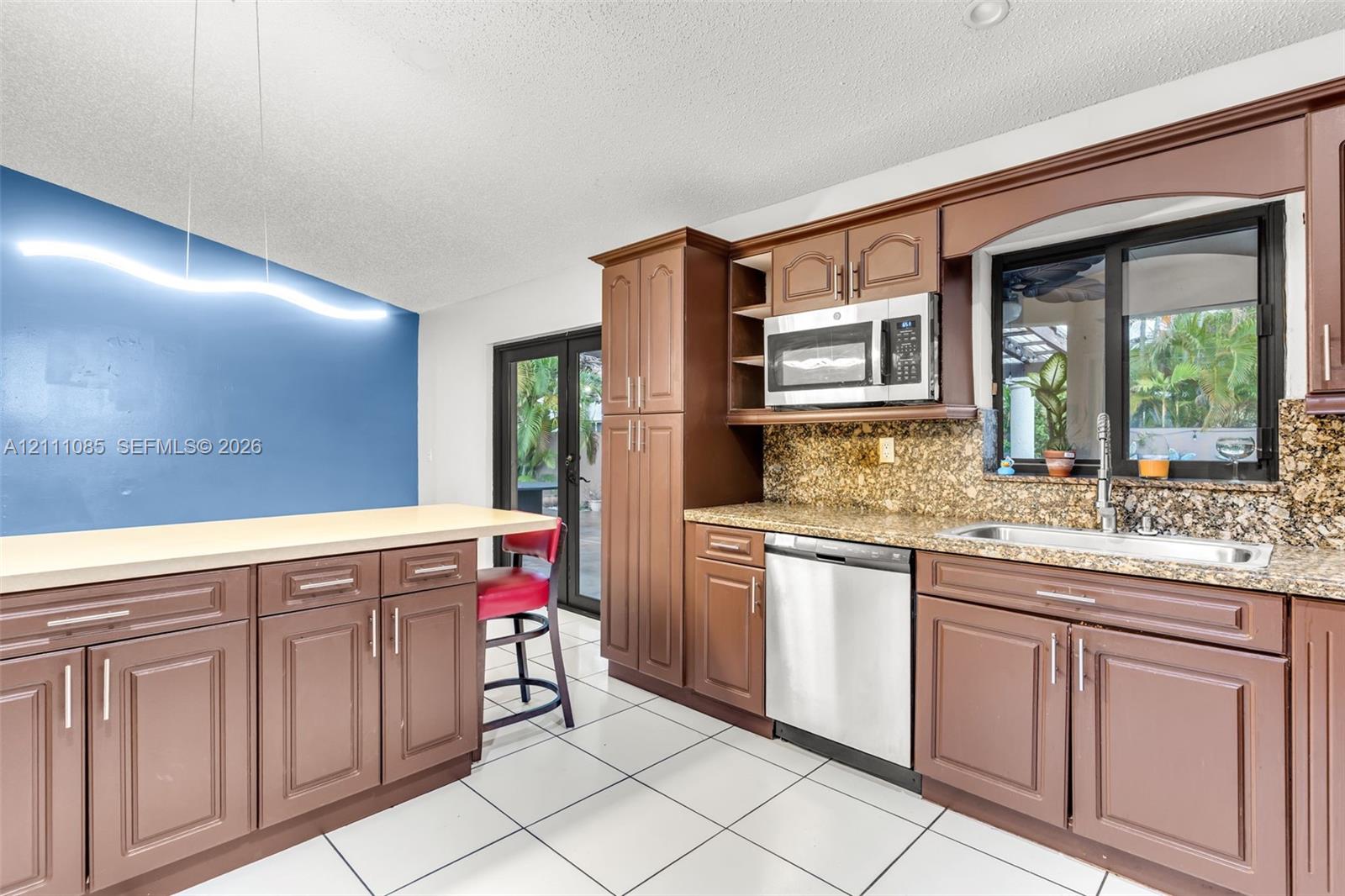 Kitchen featuring wood cabinetry, stone countertops, stainless steel appliances, ceramic tile flooring, and integrated linear lighting
