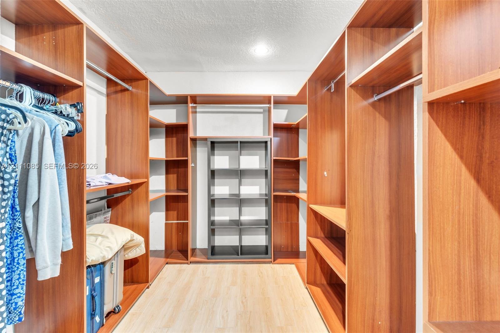 Custom walk-in closet featuring extensive wood-finish shelving, multiple hanging rods, and light wood-finish flooring