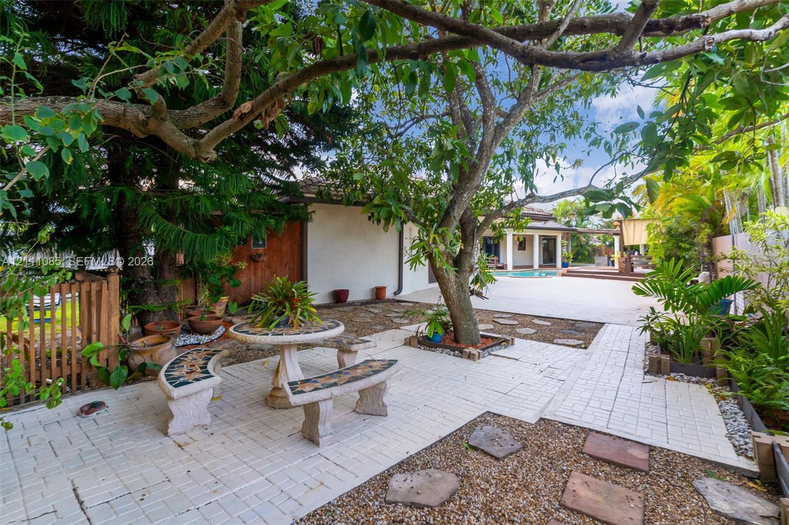 Paver patio featuring integrated stone seating, gravel landscaping, mature trees, and an in-ground pool
