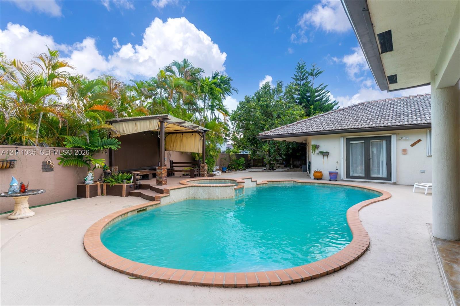 Free-form pool with brick coping and integrated spa, stucco-finished gazebo with elevated deck, and extensive paved patio area