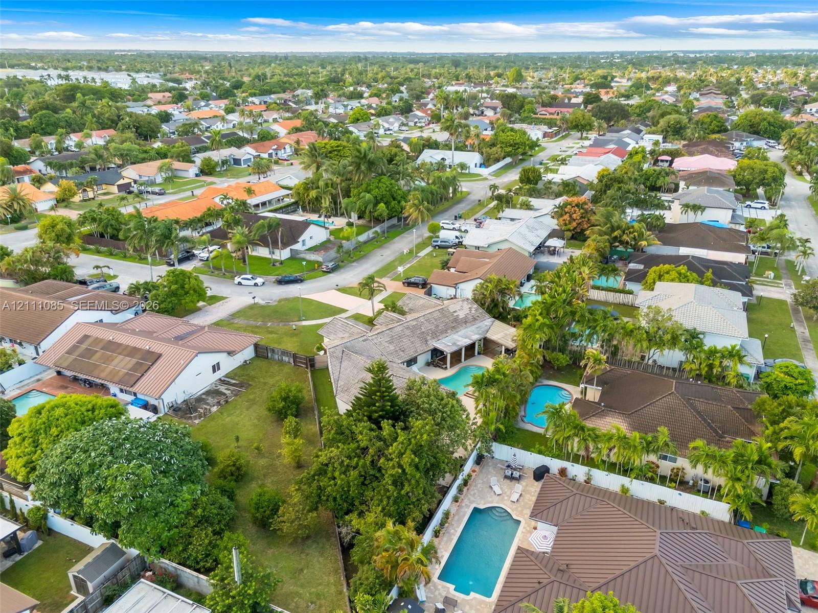 Aerial perspective of a suburban neighborhood featuring residential homes with tile roofs, established tree canopy, and private swimming pools