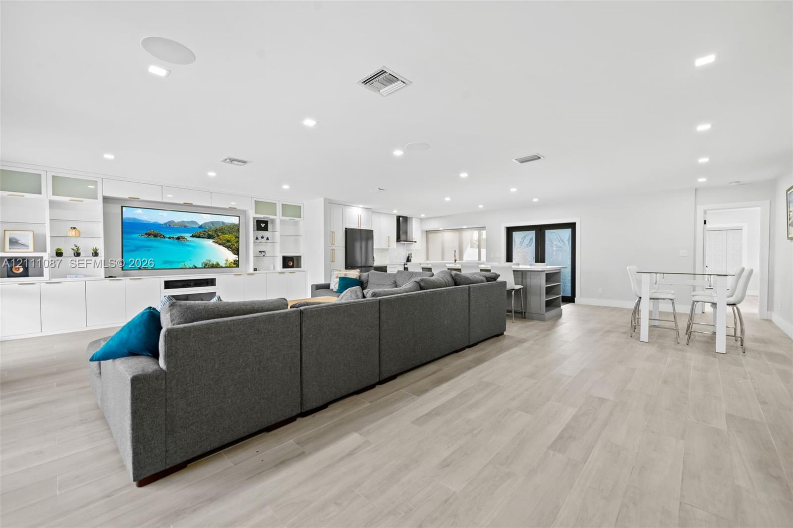 Open-concept living space featuring wood-finish flooring, recessed lighting, and custom floor-to-ceiling built-in cabinetry with integrated media center