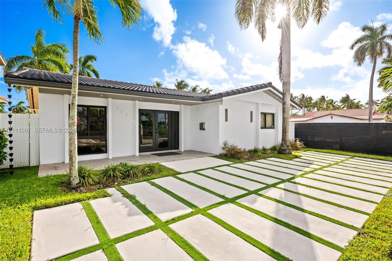 Single-story exterior featuring white stucco siding, a tiled roof, a geometric concrete paver driveway, double glass entry doors, and large-format window frames