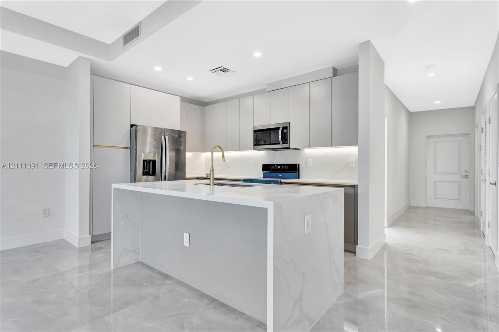 Modern kitchen featuring flat-panel cabinetry, a waterfall-edge stone island, polished tile flooring, stainless steel appliances, and under-cabinet lighting