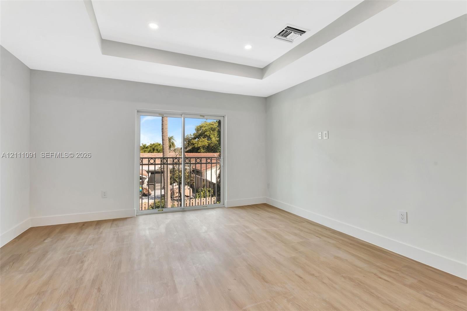 Tray ceiling with recessed lighting, wood-finish flooring, and sliding glass door with wrought iron balcony railing