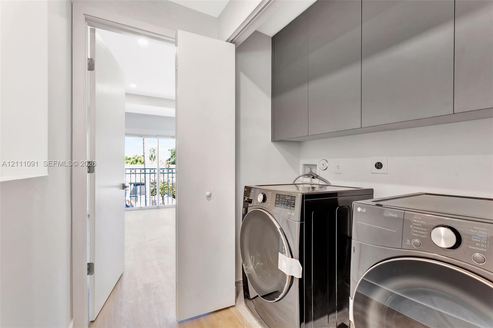 Laundry space featuring flat-panel gray cabinetry, wood-finish flooring, and a swinging door leading to a balcony