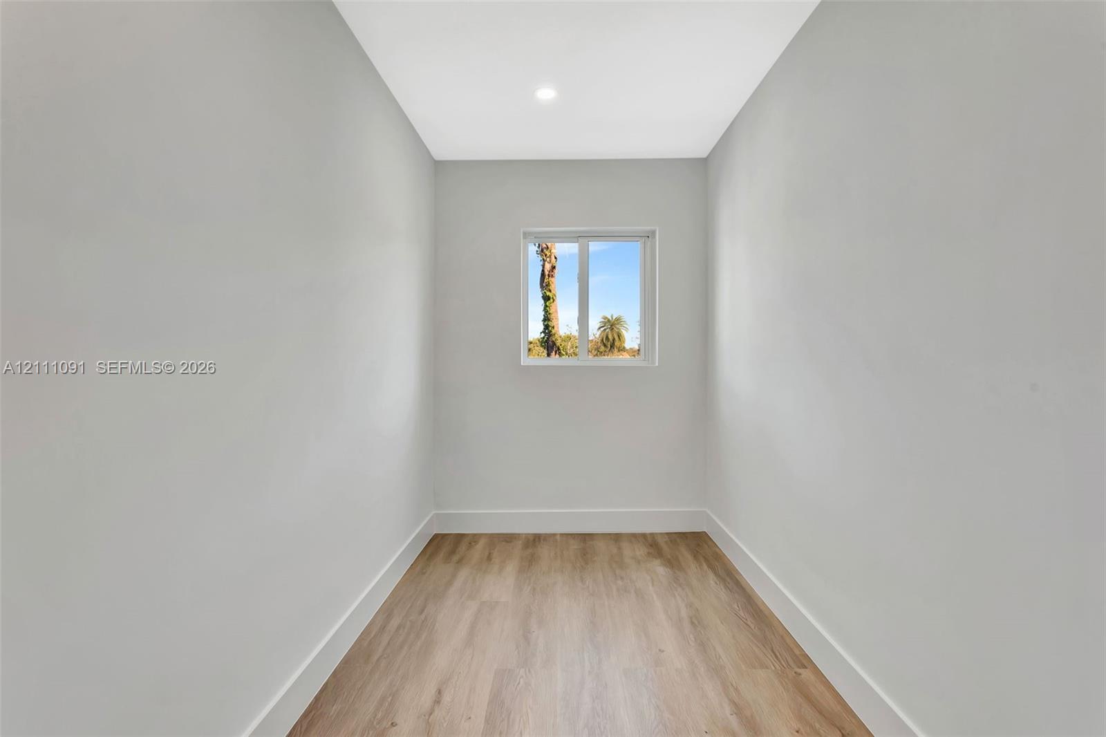 Neutral-toned interior space featuring wood-finish flooring, recessed lighting, and a square window