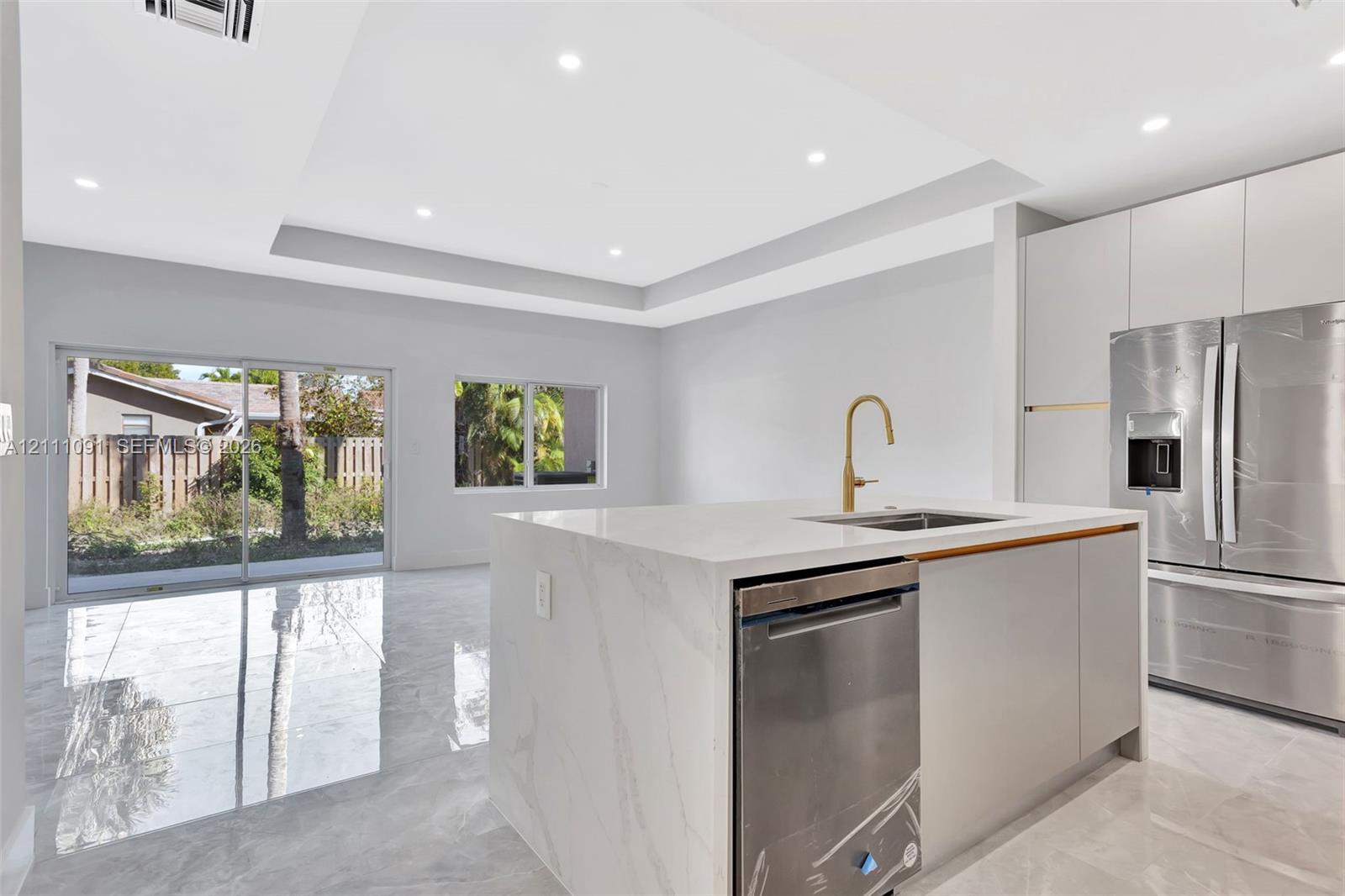 Kitchen featuring a center island with a solid surface countertop, recessed ceiling tray, polished tile flooring, flat-panel cabinetry, and stainless steel appliances