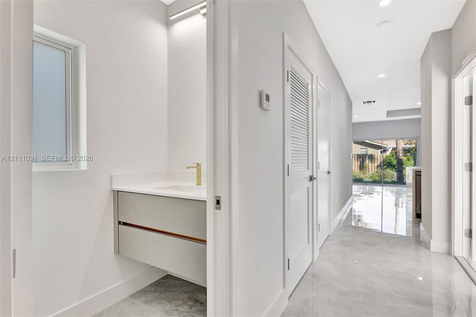 Floating vanity with integrated countertop and gold-tone faucet, complemented by stone-finish tile flooring and recessed lighting throughout