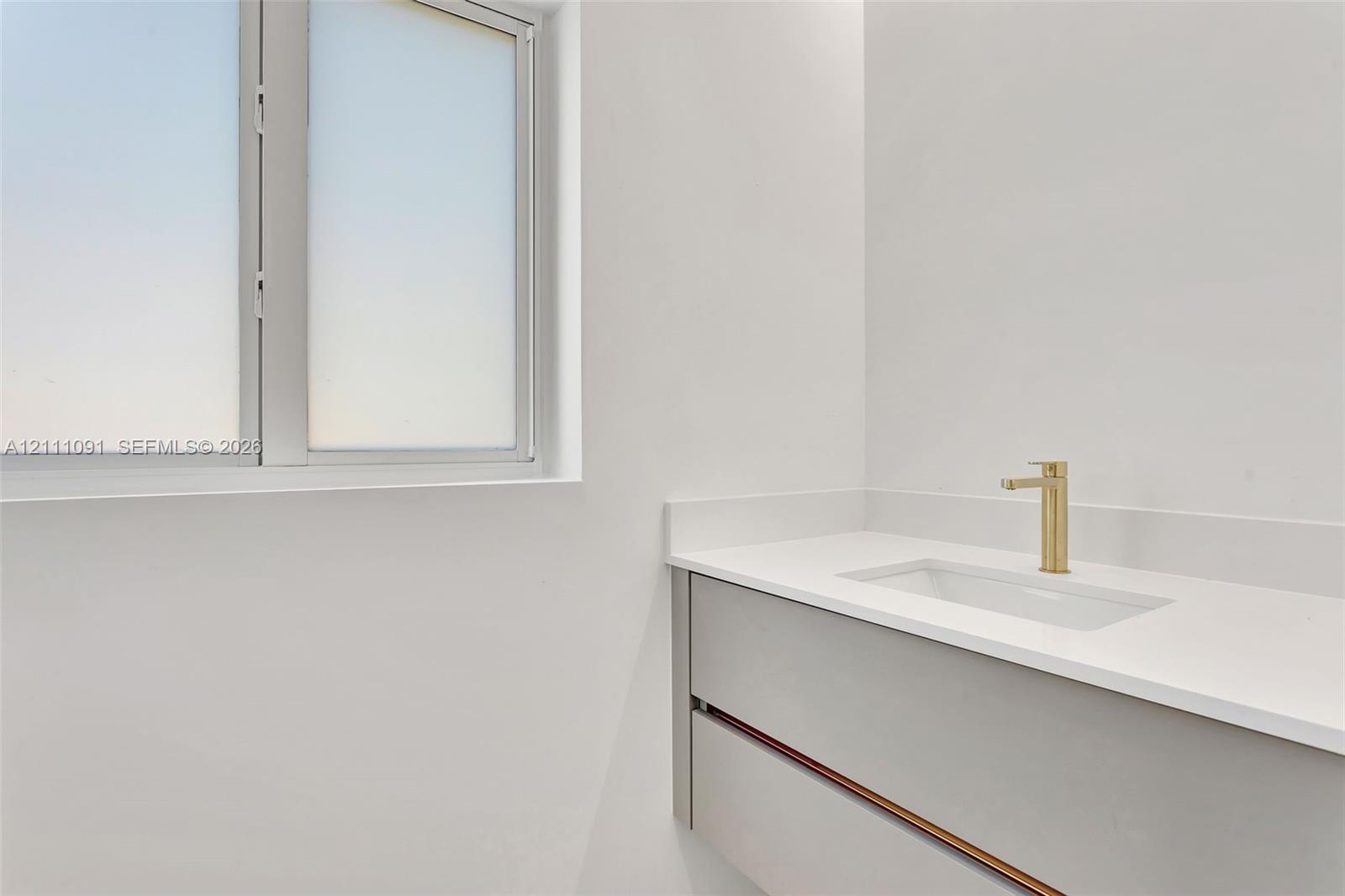 Modern floating vanity with a light gray finish, solid surface countertop, rectangular undermount sink, and brass-tone faucet