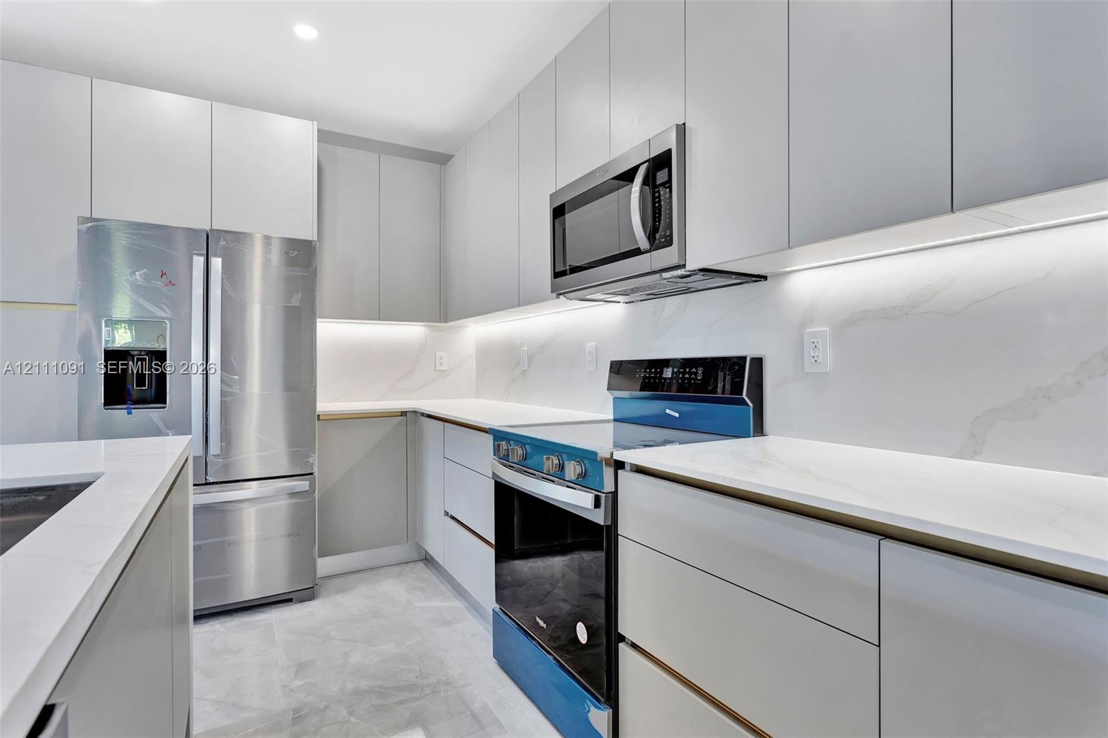 Kitchen featuring flat-panel cabinetry, stone-surface countertops, full-height stone backsplash, under-cabinet lighting, and stainless steel appliances