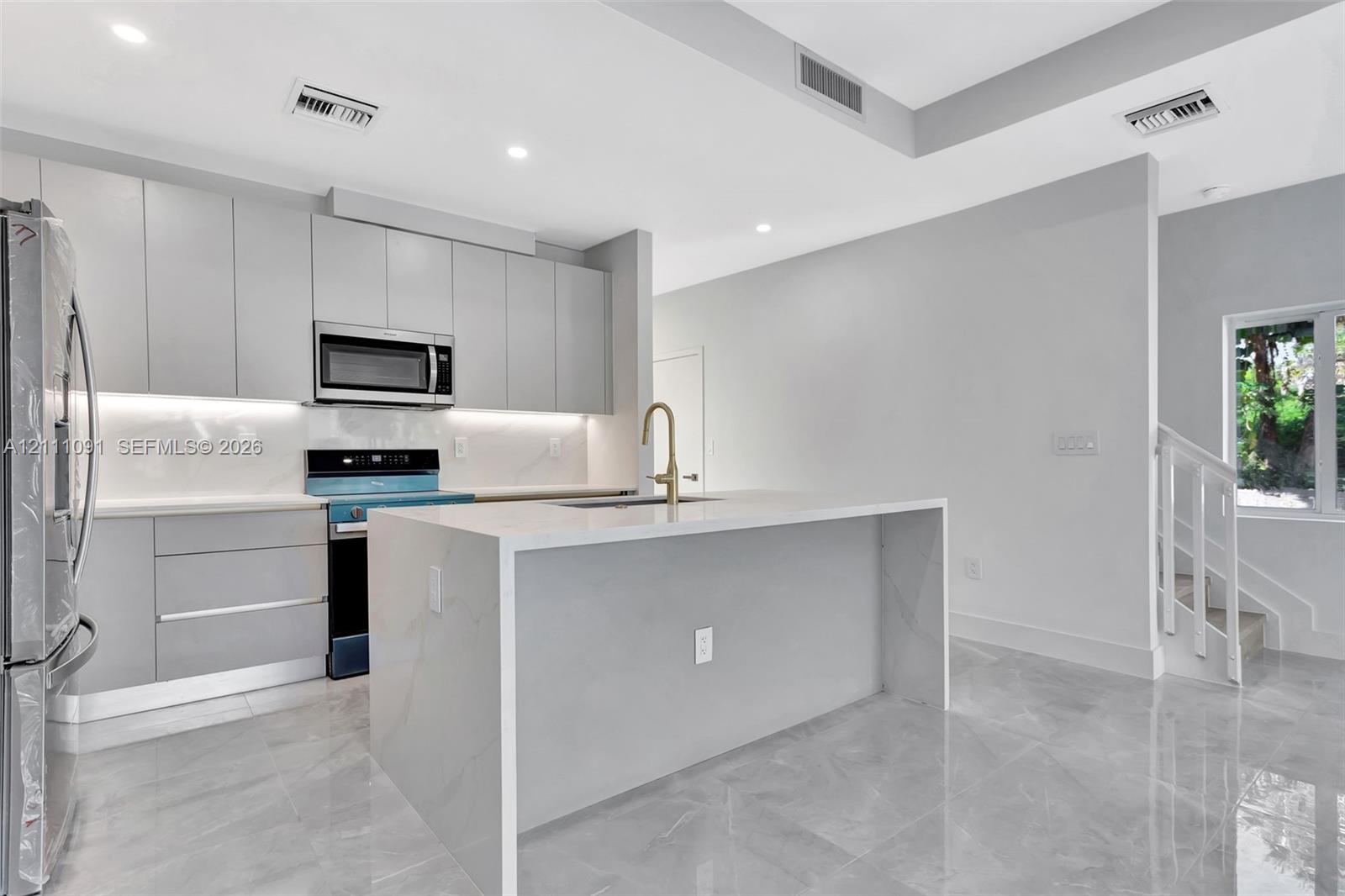 Contemporary kitchen featuring high-gloss cabinetry, a waterfall-edge island, stone-finish countertops, recessed lighting, and large-format tile flooring