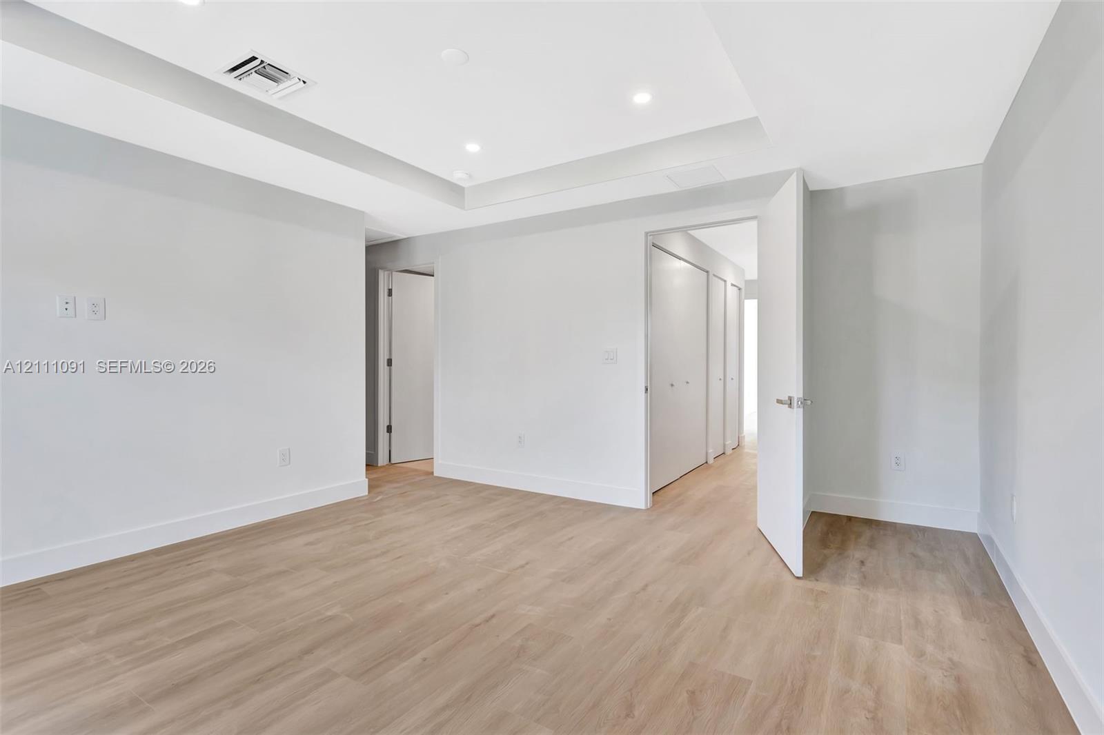Room featuring recessed lighting, tray ceiling, wood-finish flooring, and built-in closet storage