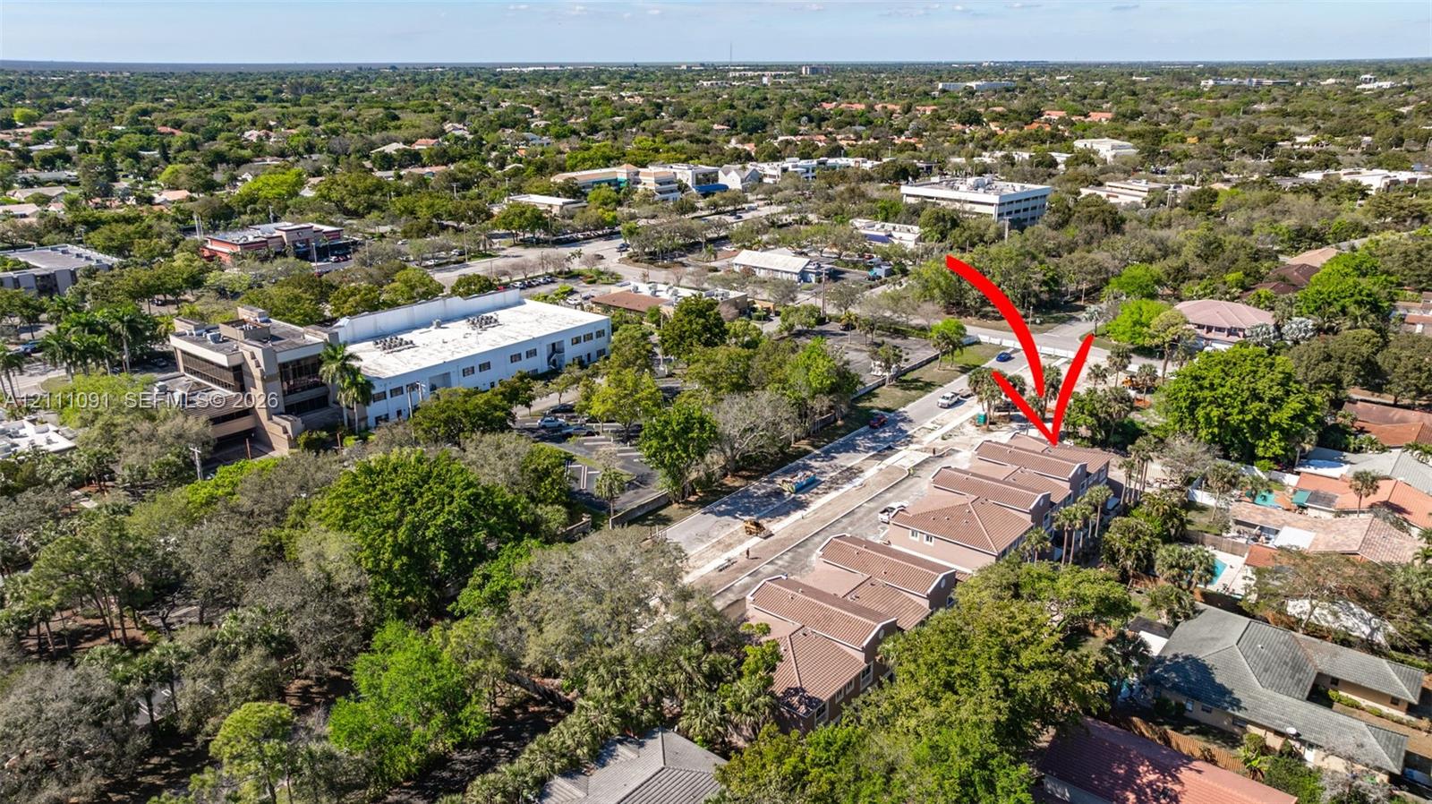 Aerial perspective of a multi-unit property featuring a shingled roof, stucco exterior, paved driveway, and mature landscaping