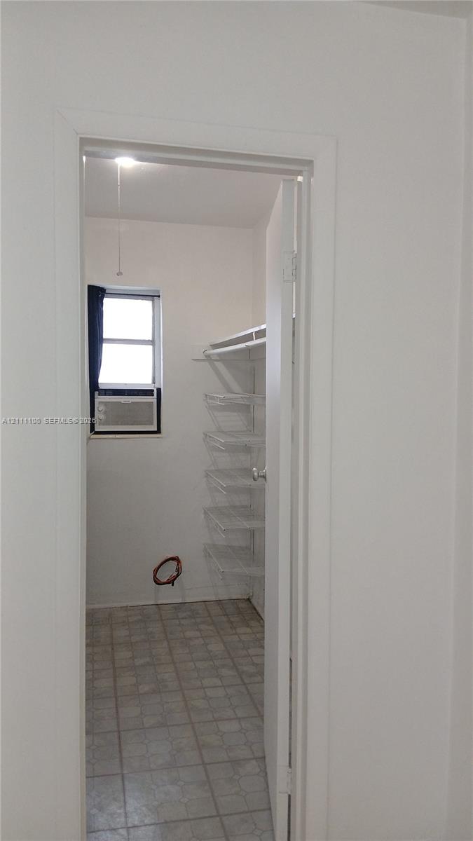 Storage room featuring tile flooring, a window, integrated wall shelving, and a hanging rod