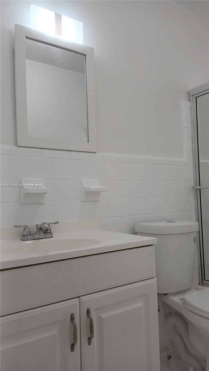 Bathroom vanity with a white cabinet, integrated sink, metal faucet, and wall-mounted mirror, featuring white subway tile wall surround