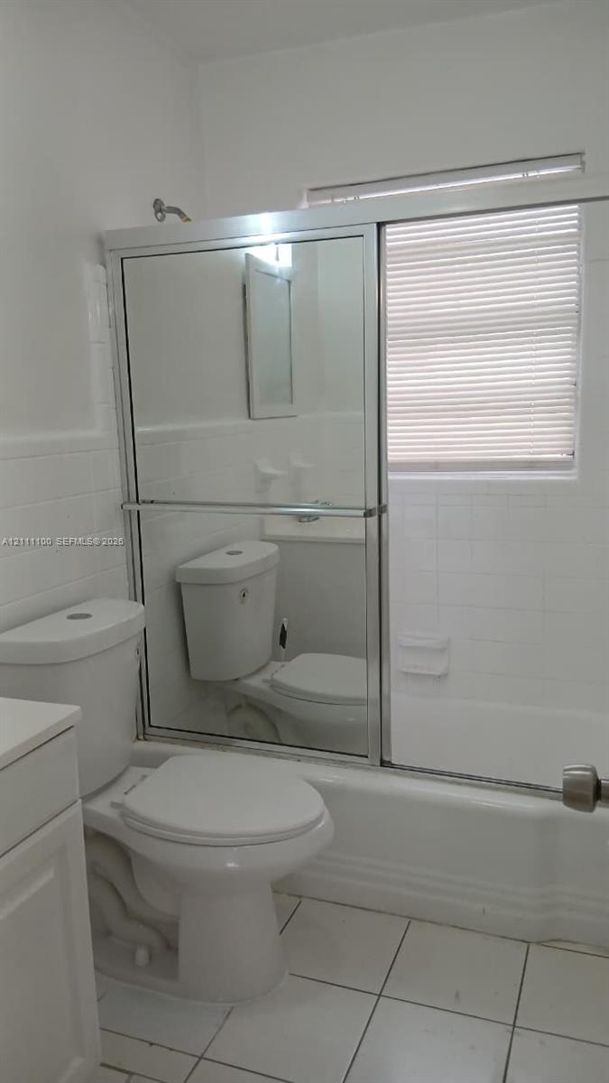 Full bathroom featuring white ceramic wall tiling, a combination bathtub and shower with a mirrored sliding enclosure, and white floor tiling