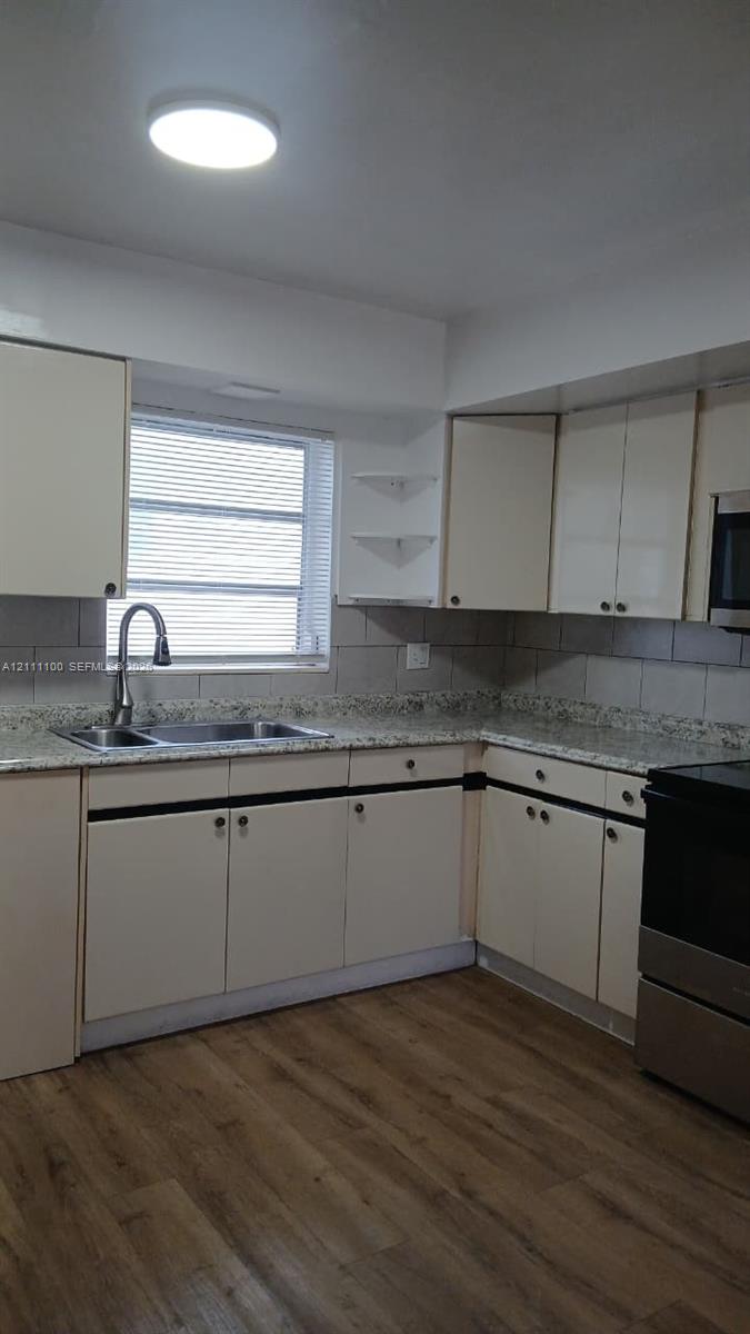 Kitchen featuring stone-finish countertops, wood-finish flooring, undermount dual-basin sink with arched faucet, and built-in cabinetry with open corner shelving