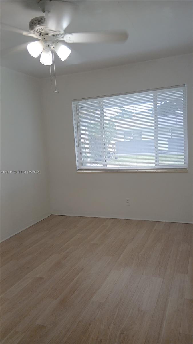 Interior space featuring light-toned wood-finish flooring, a ceiling fan with integrated lighting, and a large multi-pane window