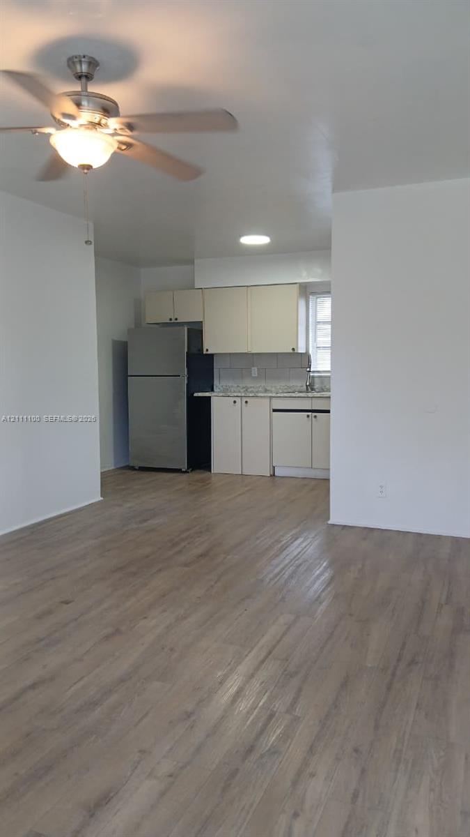 Wood-finish flooring, ceiling fan with integrated lighting, stainless steel refrigerator, solid-surface countertops, and cabinetry with minimalist hardware