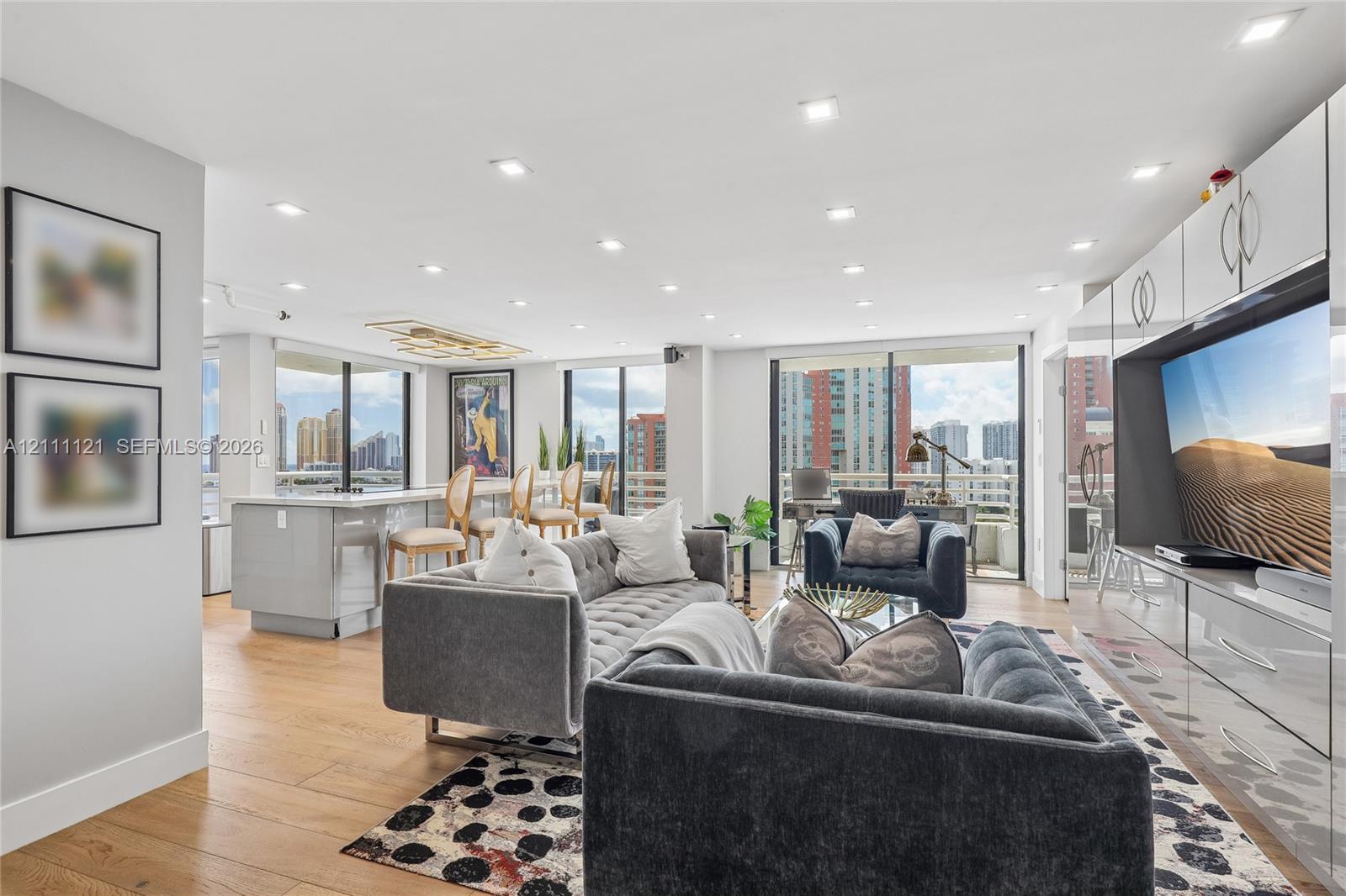 Open-concept main living area featuring wood-finish flooring, recessed lighting, floor-to-ceiling glass sliding doors, and custom built-in white cabinetry with integrated media storage