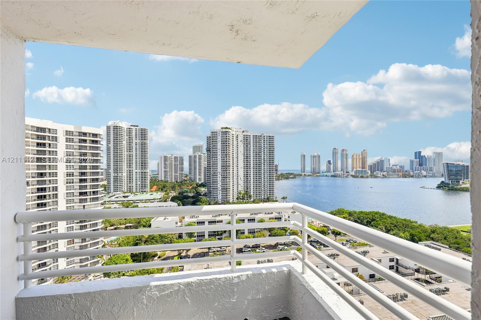 Private balcony with a white horizontal railing overlooking a cityscape, waterfront, and marina