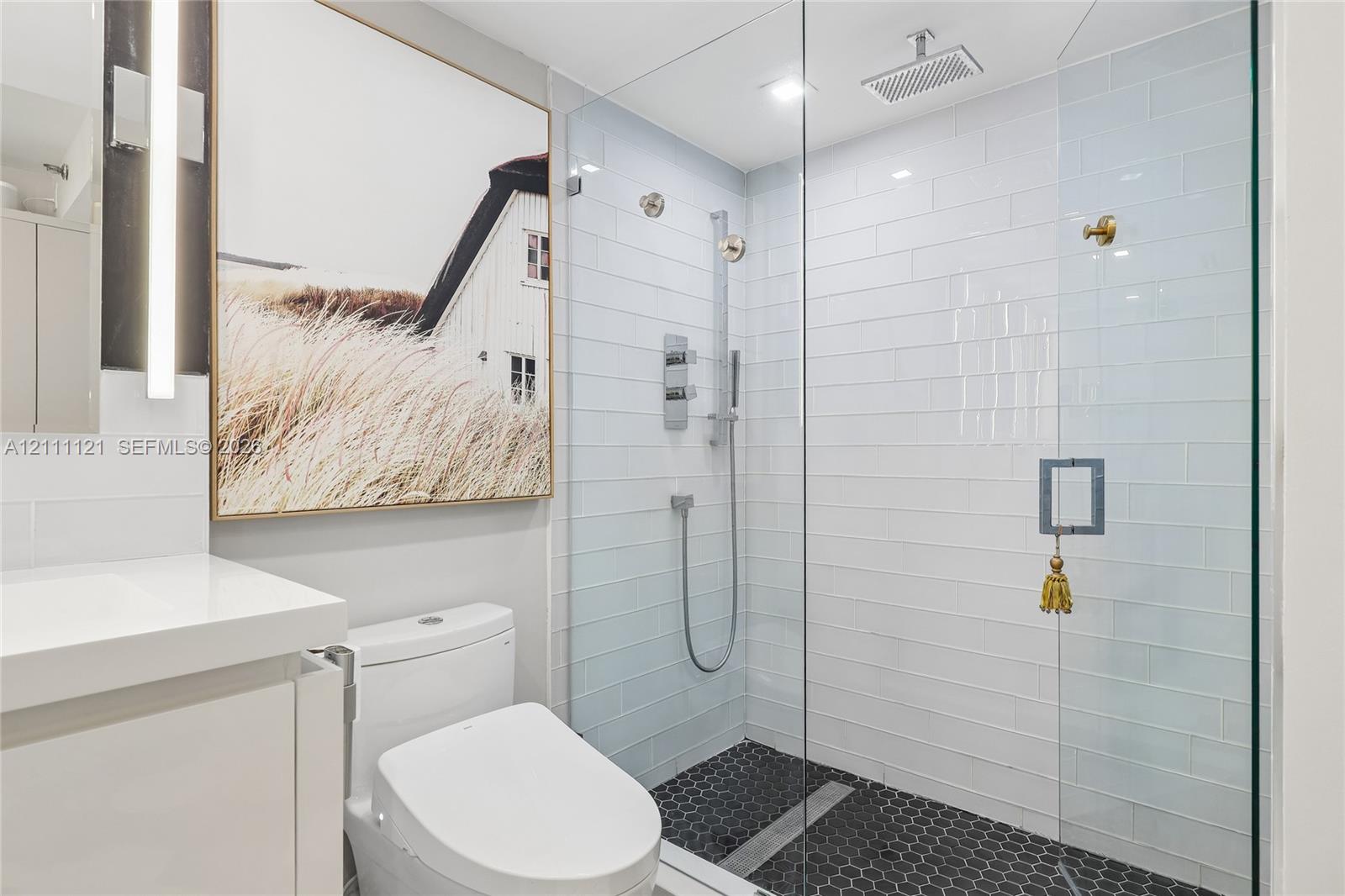 Walk-in shower featuring a frameless glass enclosure, white subway tile surround, dark hexagonal floor tiling, and a rainfall showerhead