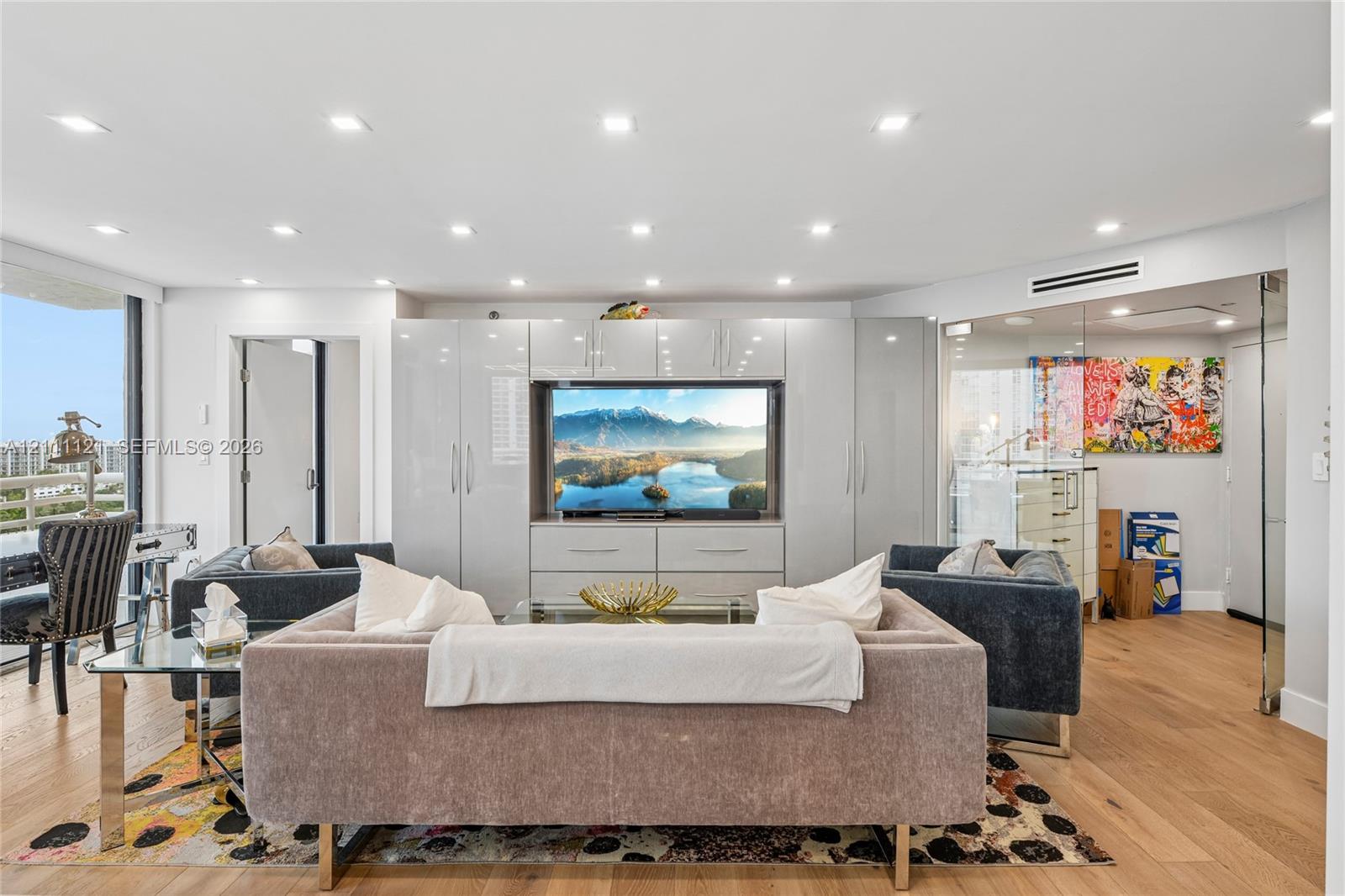 Living area featuring engineered wood-finish flooring, recessed ceiling lighting, built-in floor-to-ceiling high-gloss cabinetry, and a glass-enclosed partitioned space