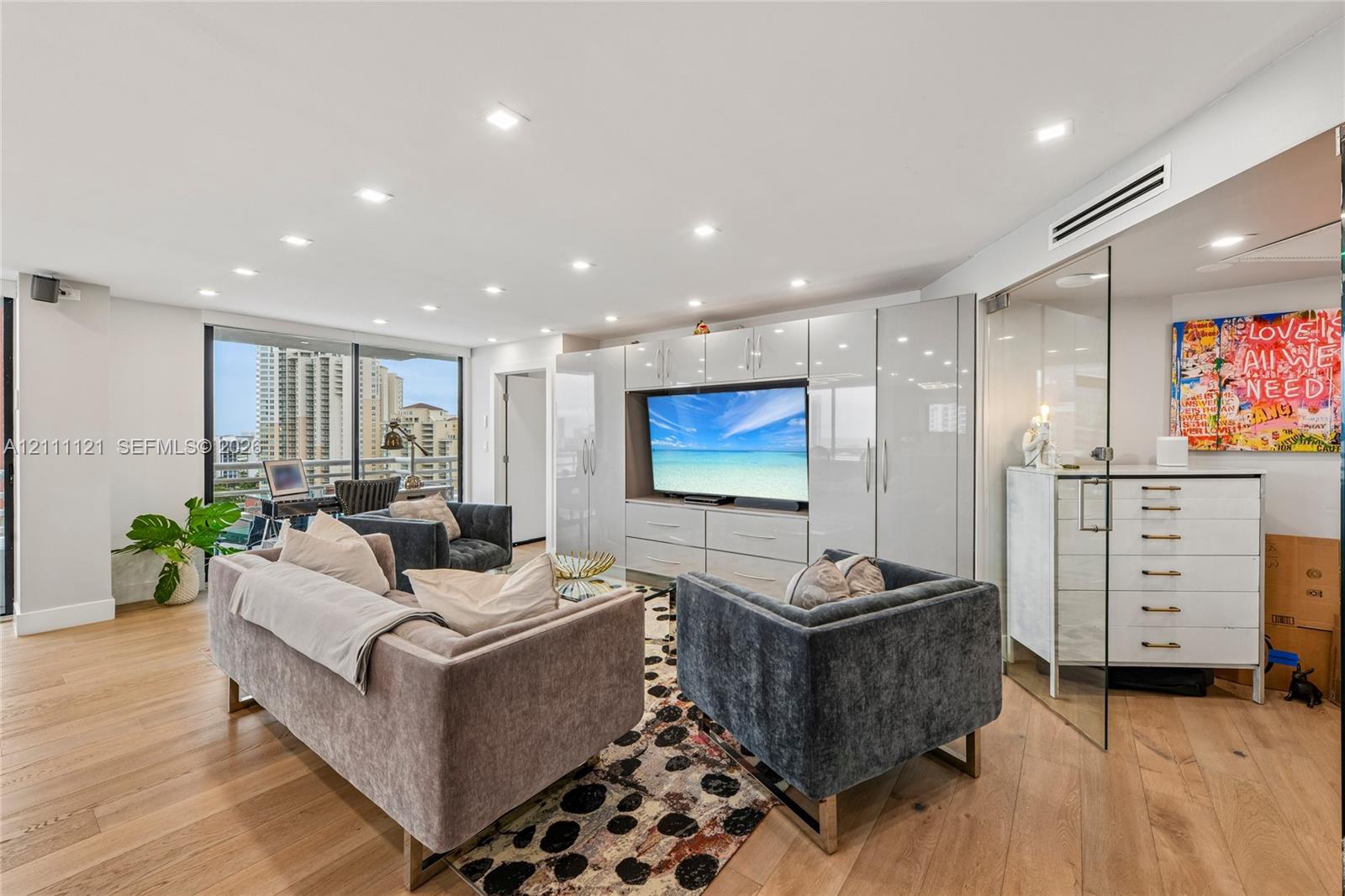 Open-concept interior featuring light wood-finish flooring, recessed lighting, floor-to-ceiling glass enclosure, and high-gloss built-in cabinetry with integrated media center